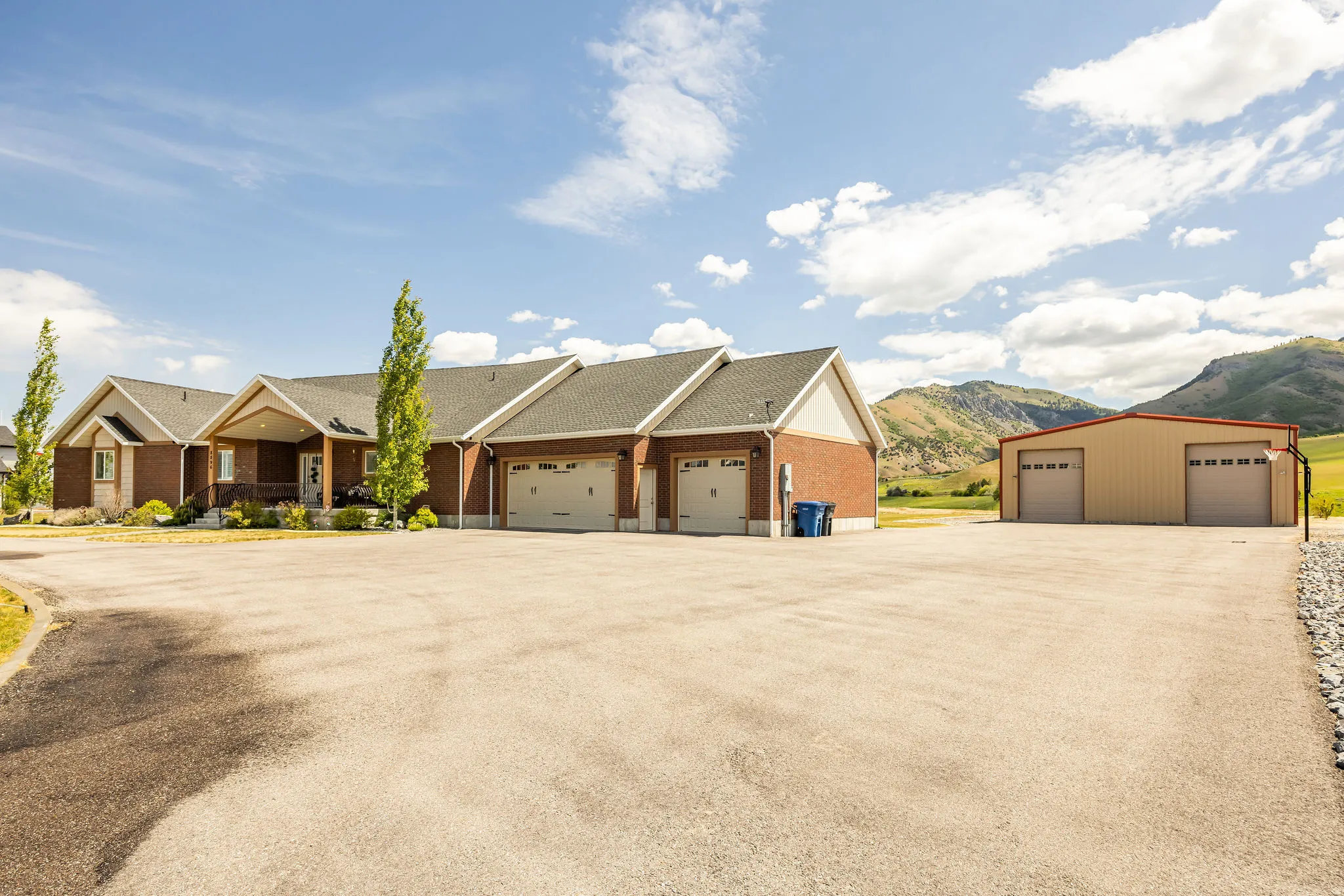 Brick exterior home with an attached multi-car garage, expansive paved driveway, and an additional detached two-bay structure, all set against a mountainous backdrop
