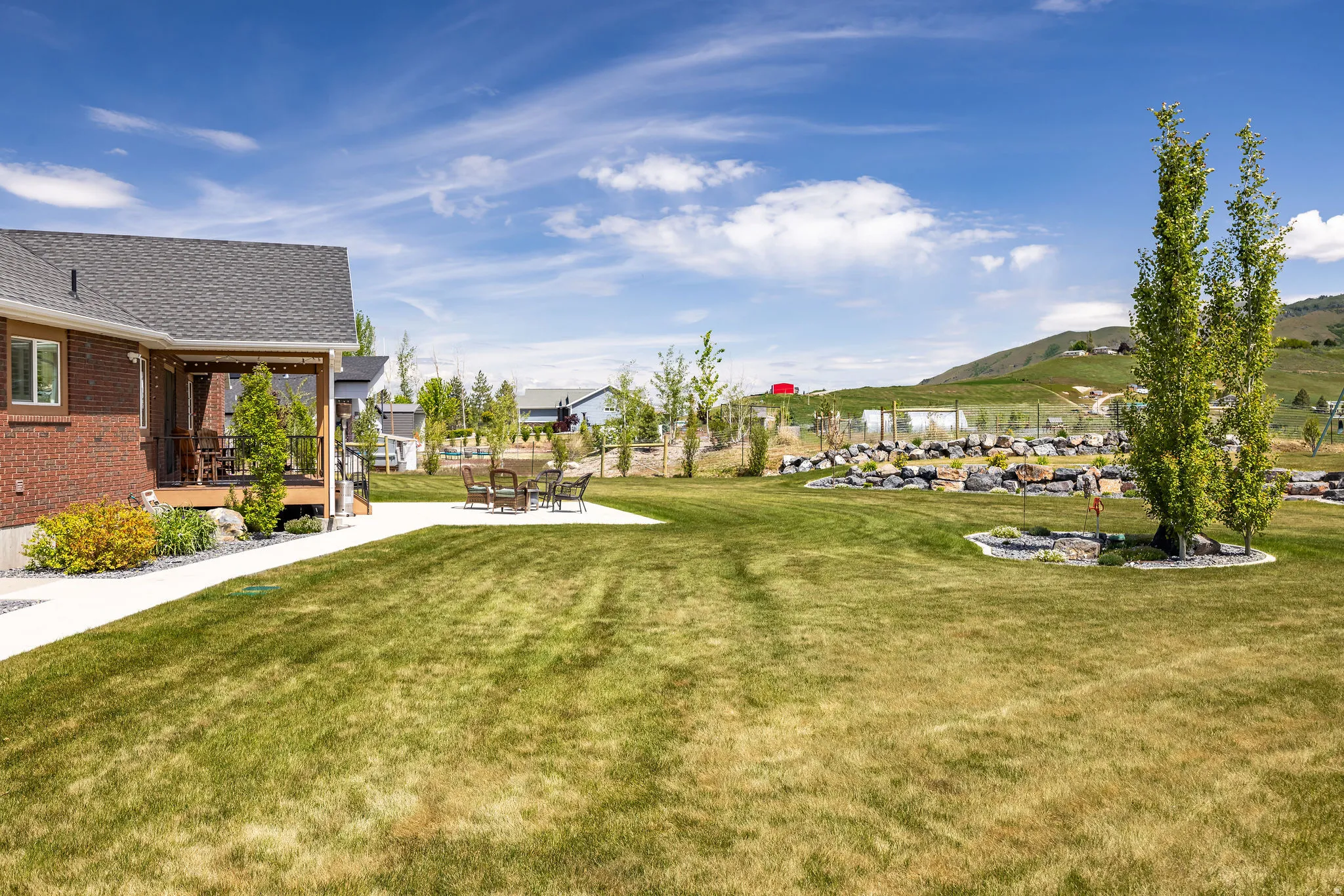 Spacious green lawn featuring a covered wood deck, concrete patio area, and decorative rock landscaping