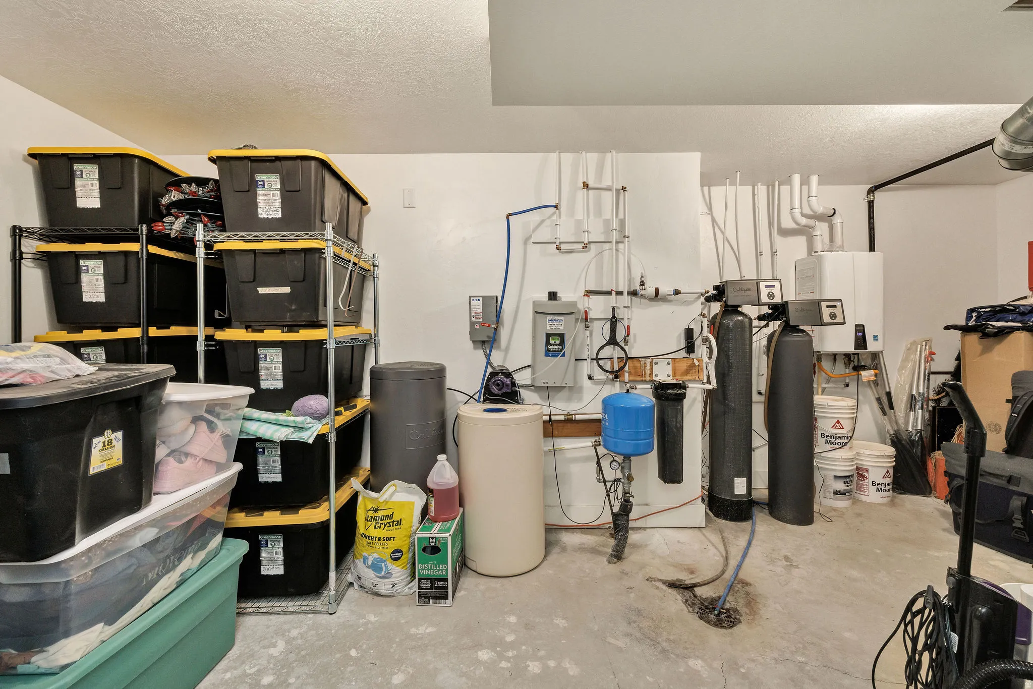 Utility room featuring a water softener system, water heater, and various plumbing installations