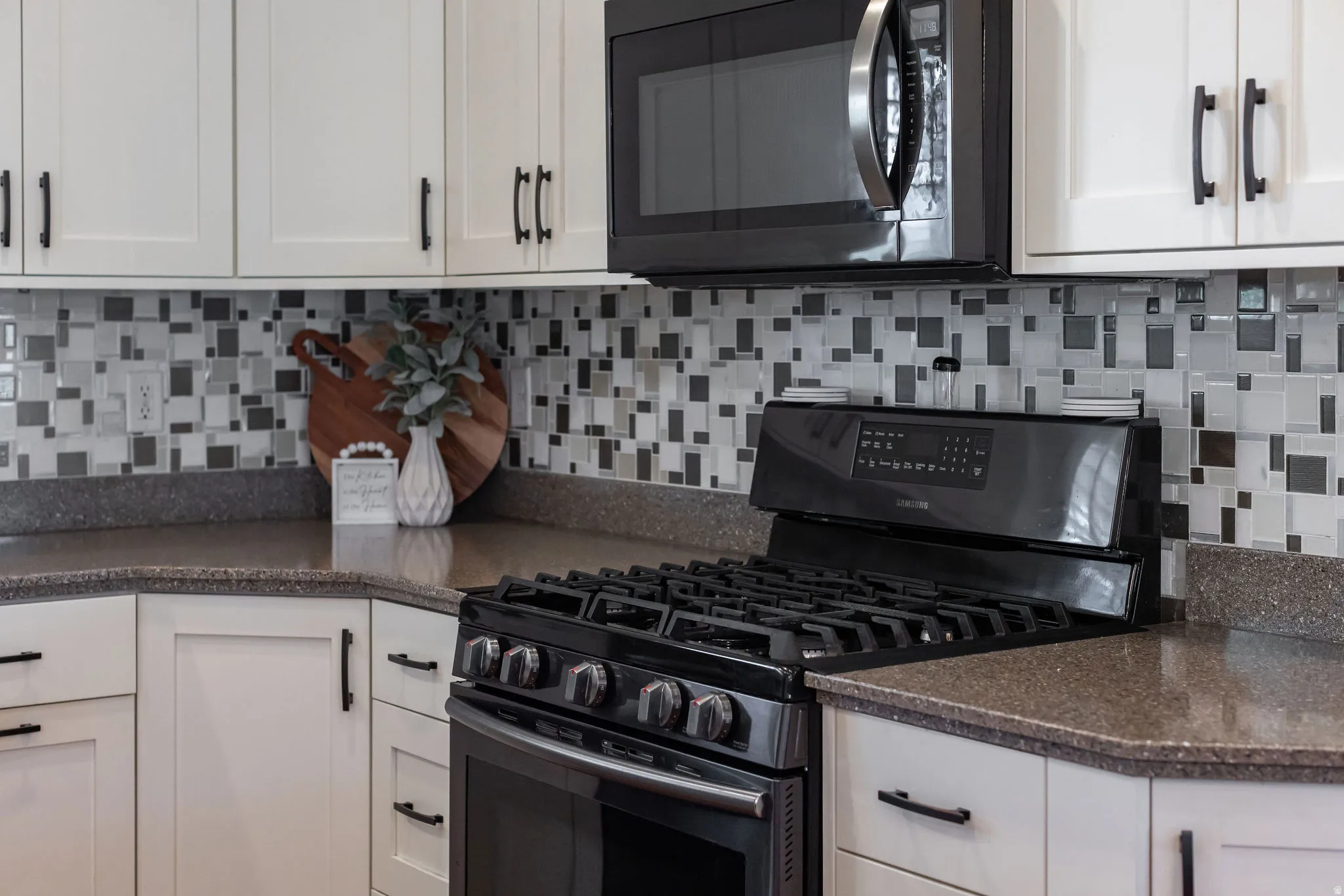 Kitchen featuring a black gas range, coordinating black microwave, speckled countertops, and white shaker-style cabinetry with matte black hardware