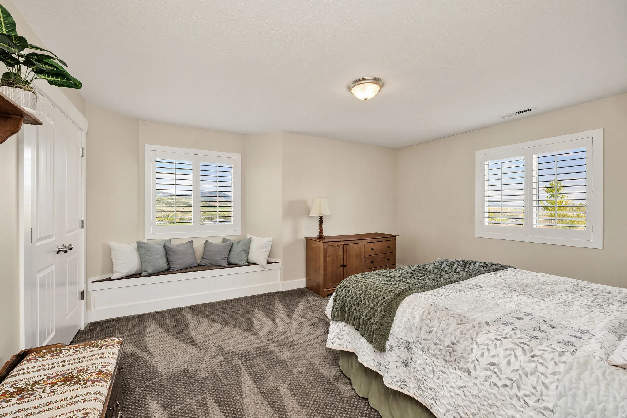 Spacious room featuring a built-in window seat, two windows with plantation shutters, neutral wall paint, and patterned carpet flooring