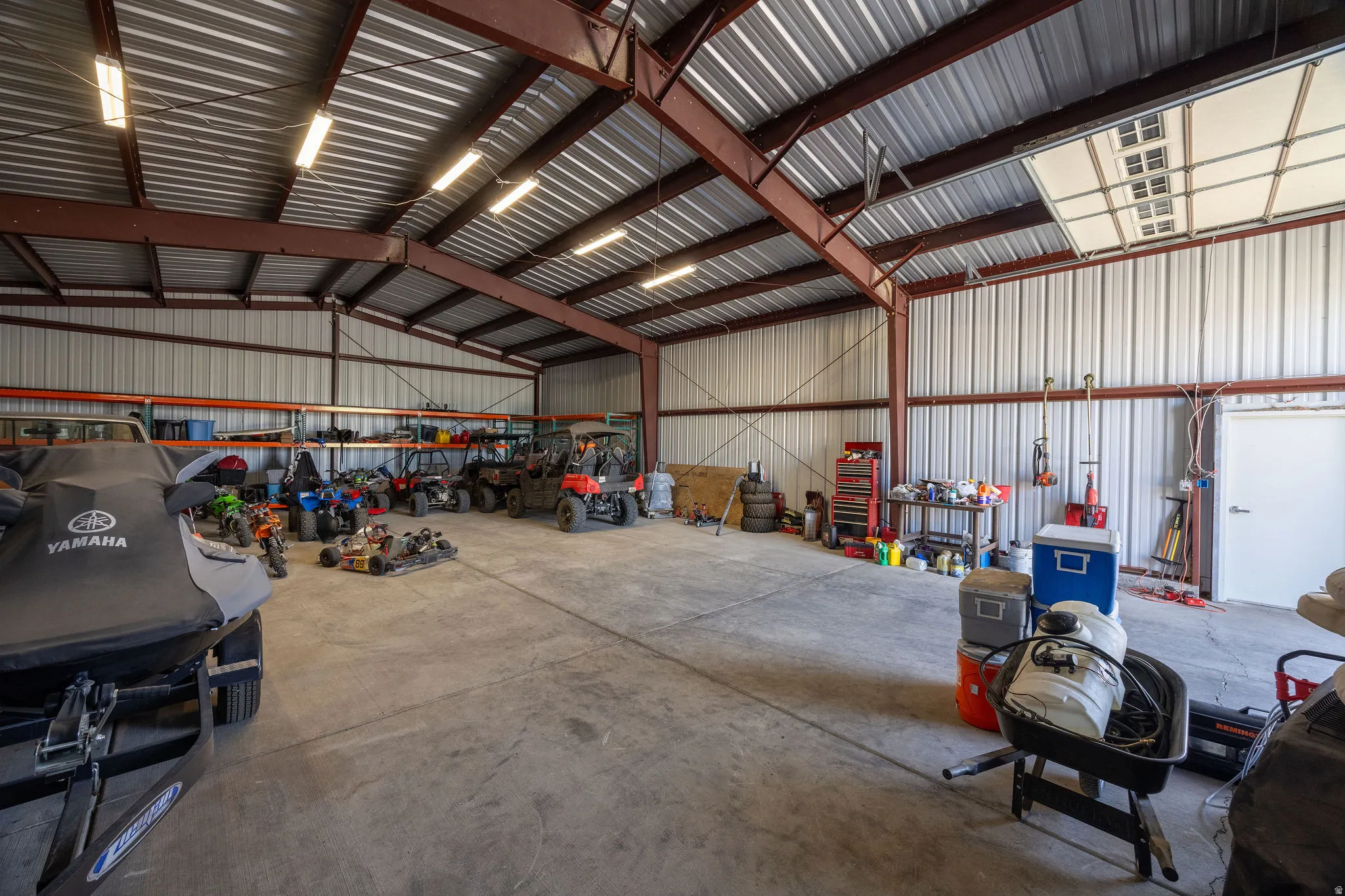 Spacious metal building featuring an open floor plan, concrete flooring, corrugated metal walls, exposed steel beams, and strip lighting fixtures