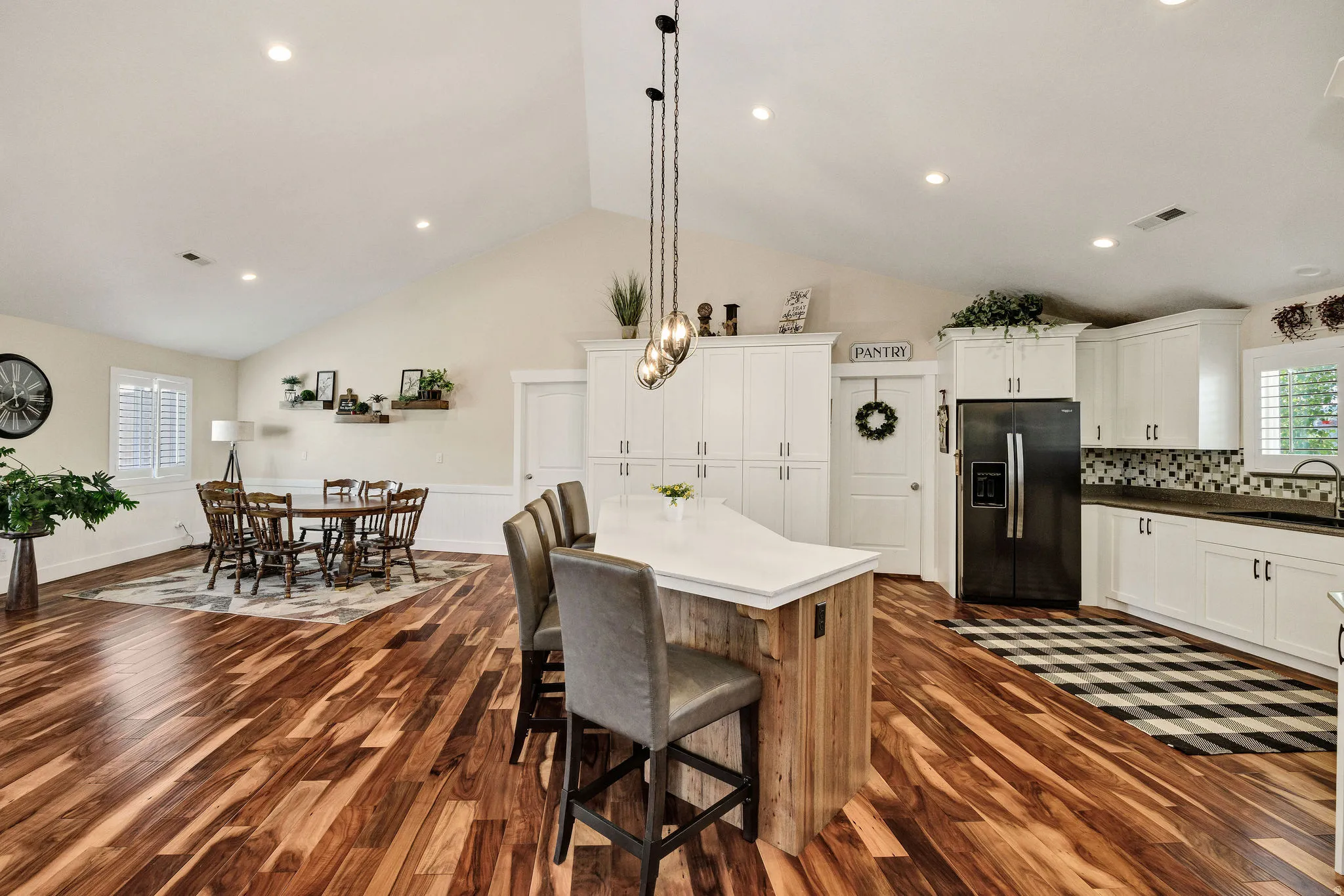 Open-concept kitchen and dining area featuring vaulted ceilings, wood-finish flooring, white cabinetry, a kitchen island with seating, and a black refrigerator