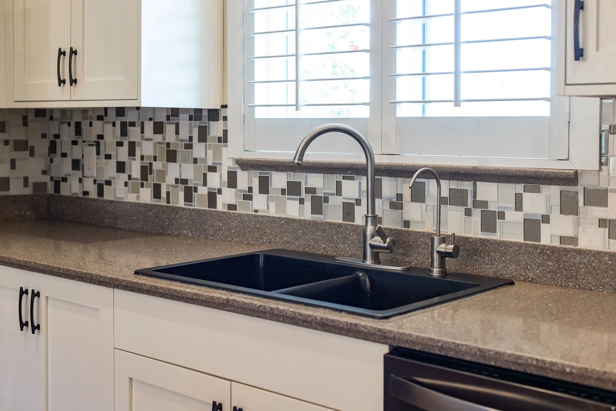 Kitchen featuring a double basin sink with a gooseneck faucet, light-toned countertops, and a mosaic tile backsplash