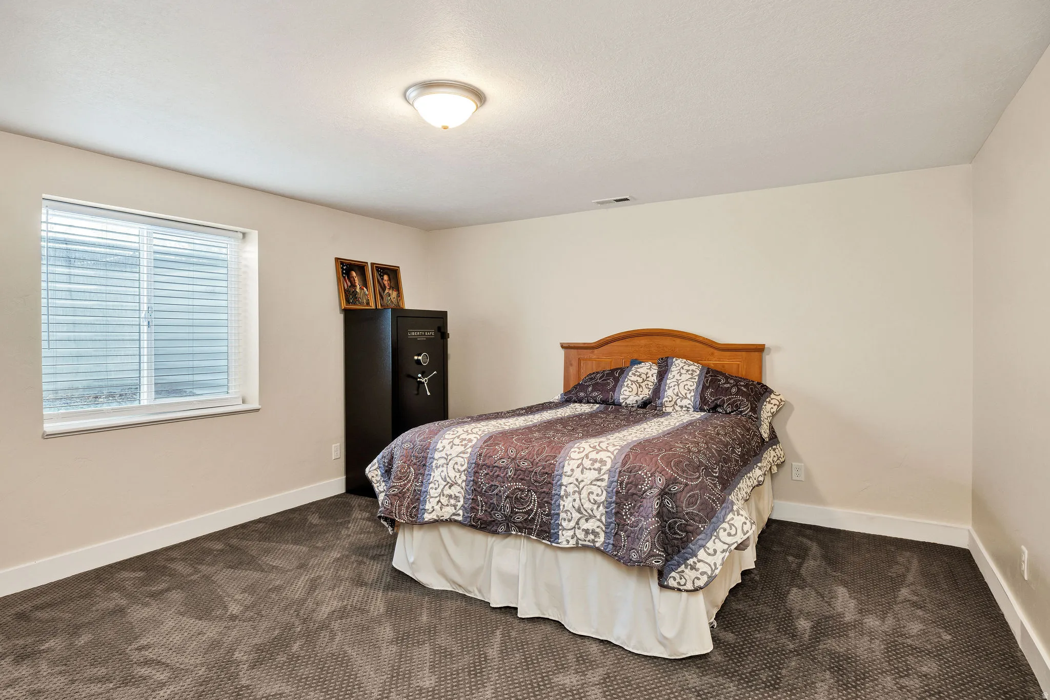 Carpeted room featuring a window with blinds, a ceiling-mounted light fixture, and light-toned walls with white baseboards