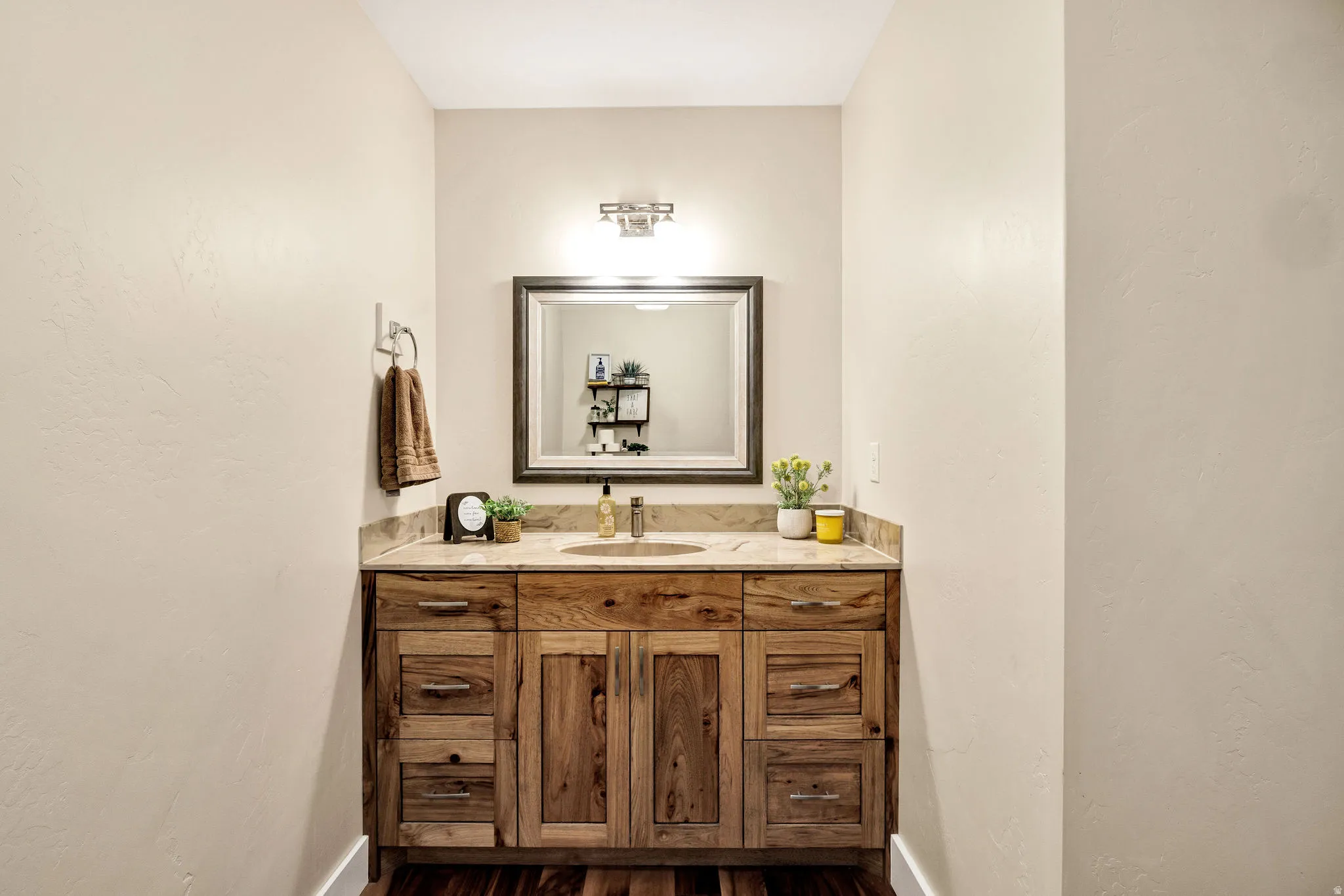 Wood-finish vanity with a single basin, stone countertop, and an overhead vanity light