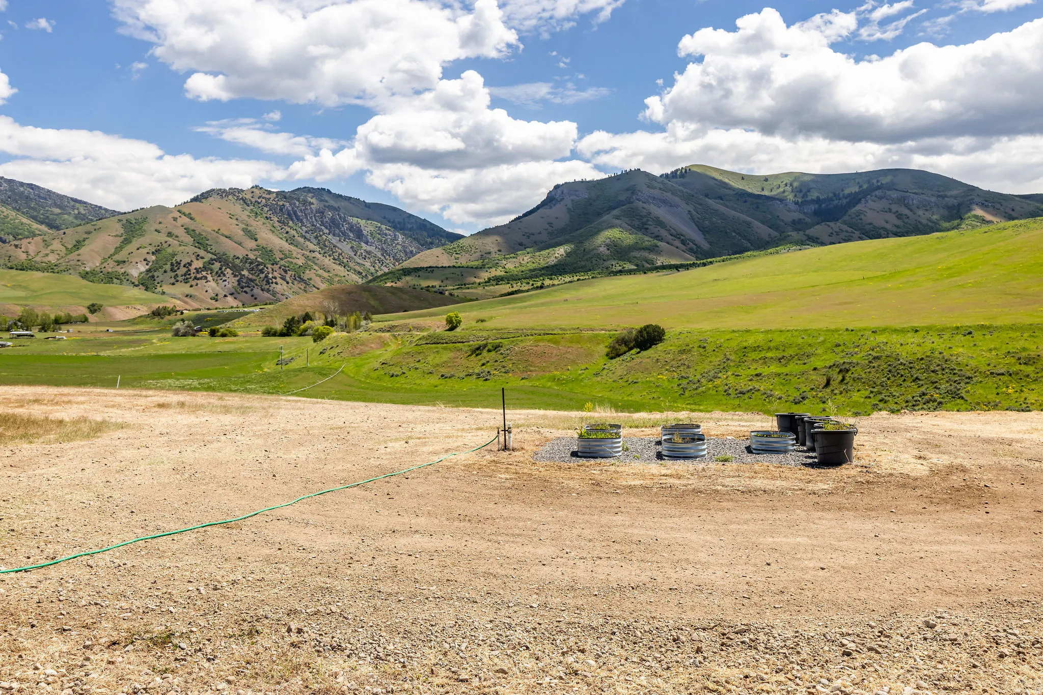 Expansive open lot featuring a gravel surface, established vegetation, and a mountainous backdrop