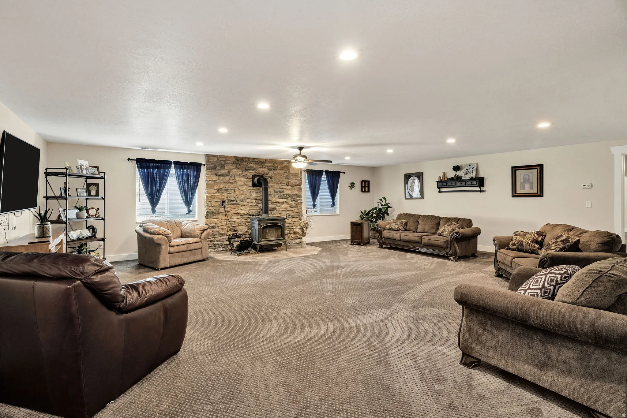 Spacious room with a stone-clad accent wall, a freestanding wood stove, recessed lighting, and a ceiling fan