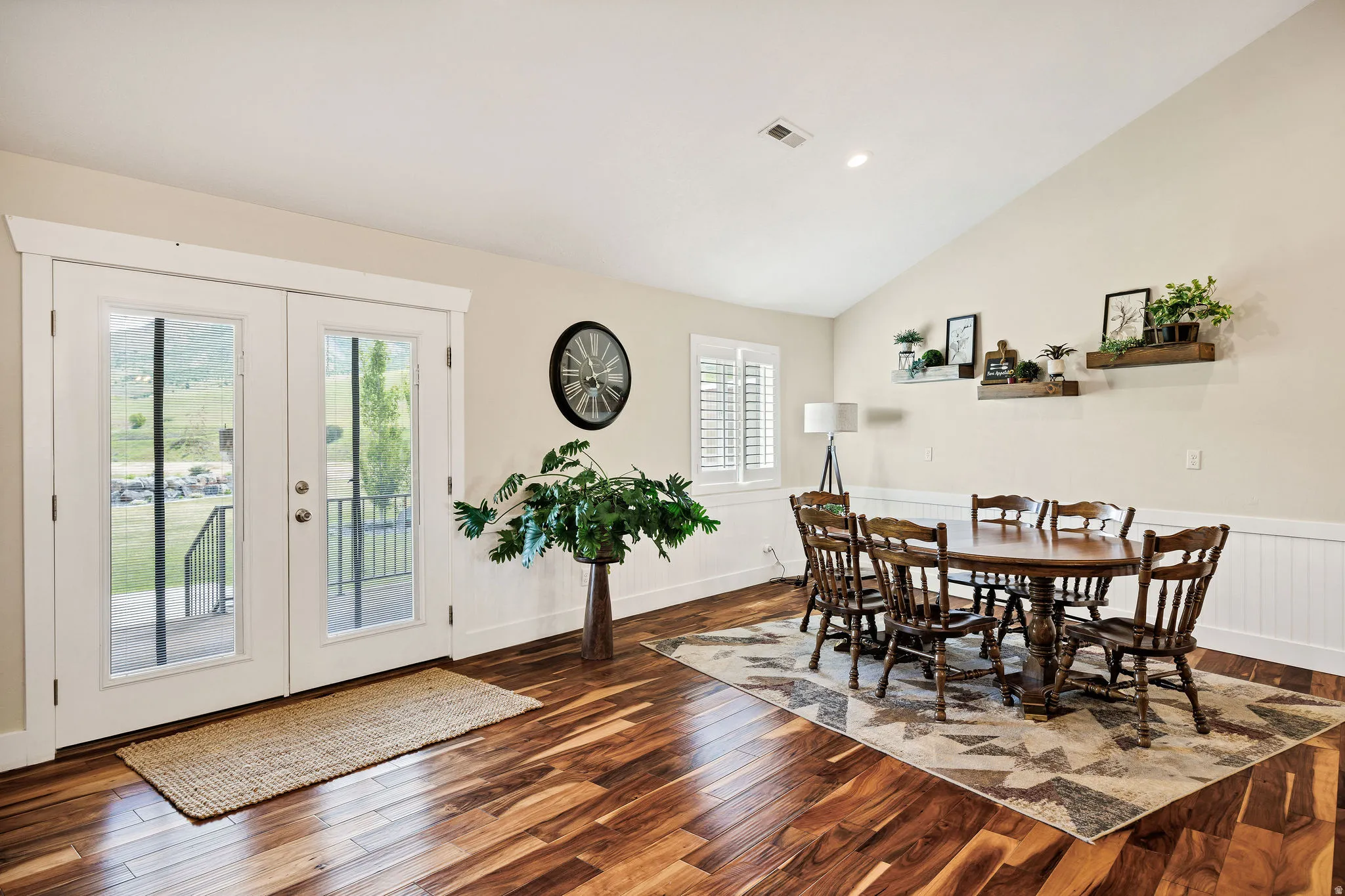 Vaulted ceiling dining area featuring wood-finish flooring, white wainscoting, and French doors opening to an exterior deck