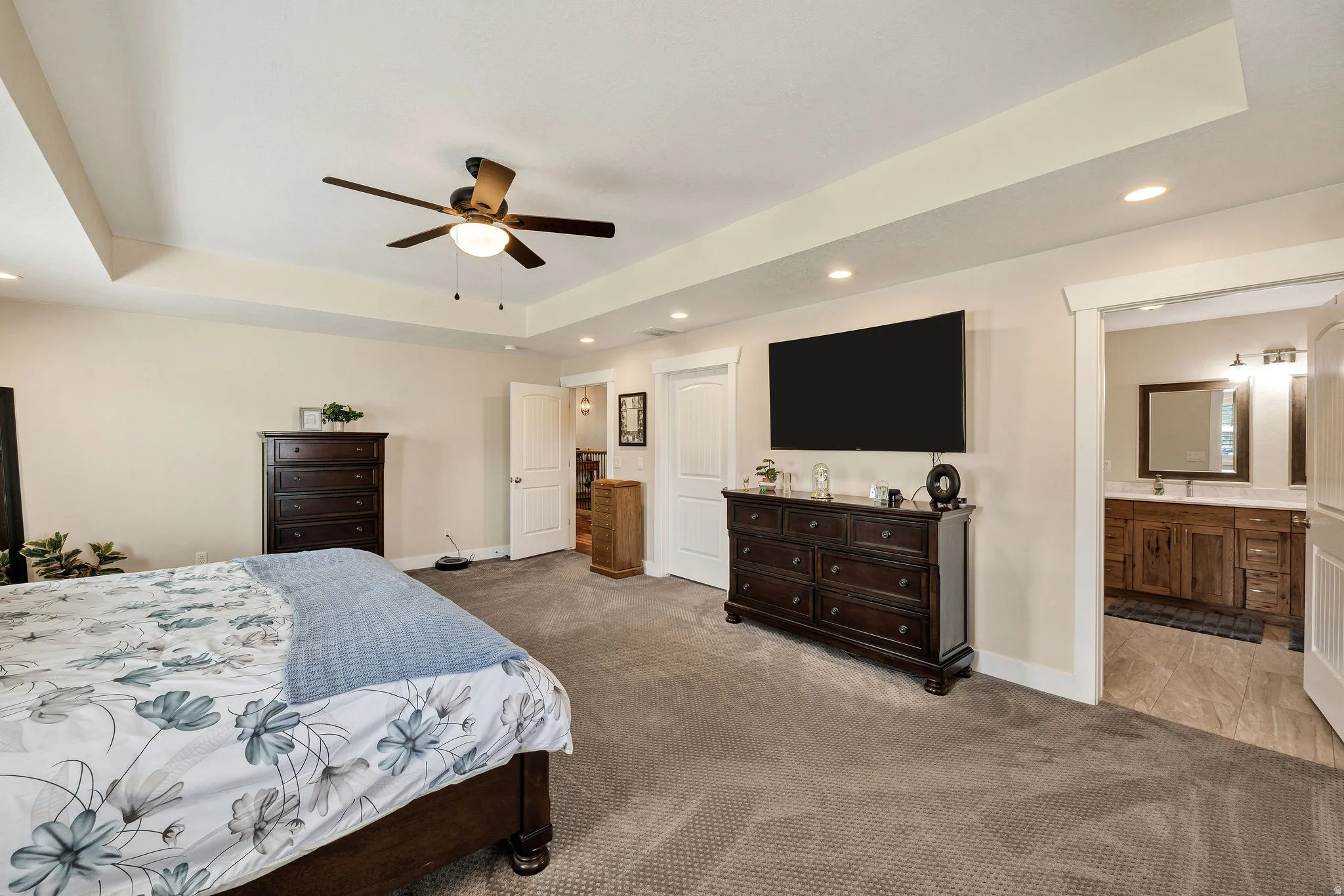 Spacious primary bedroom featuring a tray ceiling with a ceiling fan, recessed lighting, and soft carpet flooring
