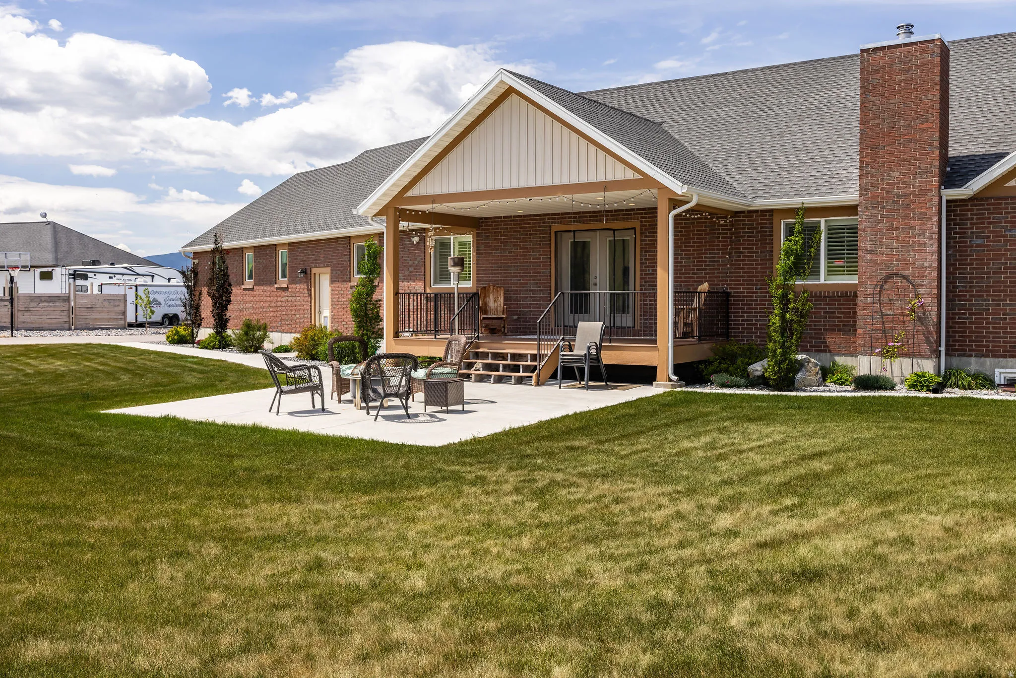 Expansive backyard featuring a large concrete patio, covered deck with wood-finish railing, and brick exterior