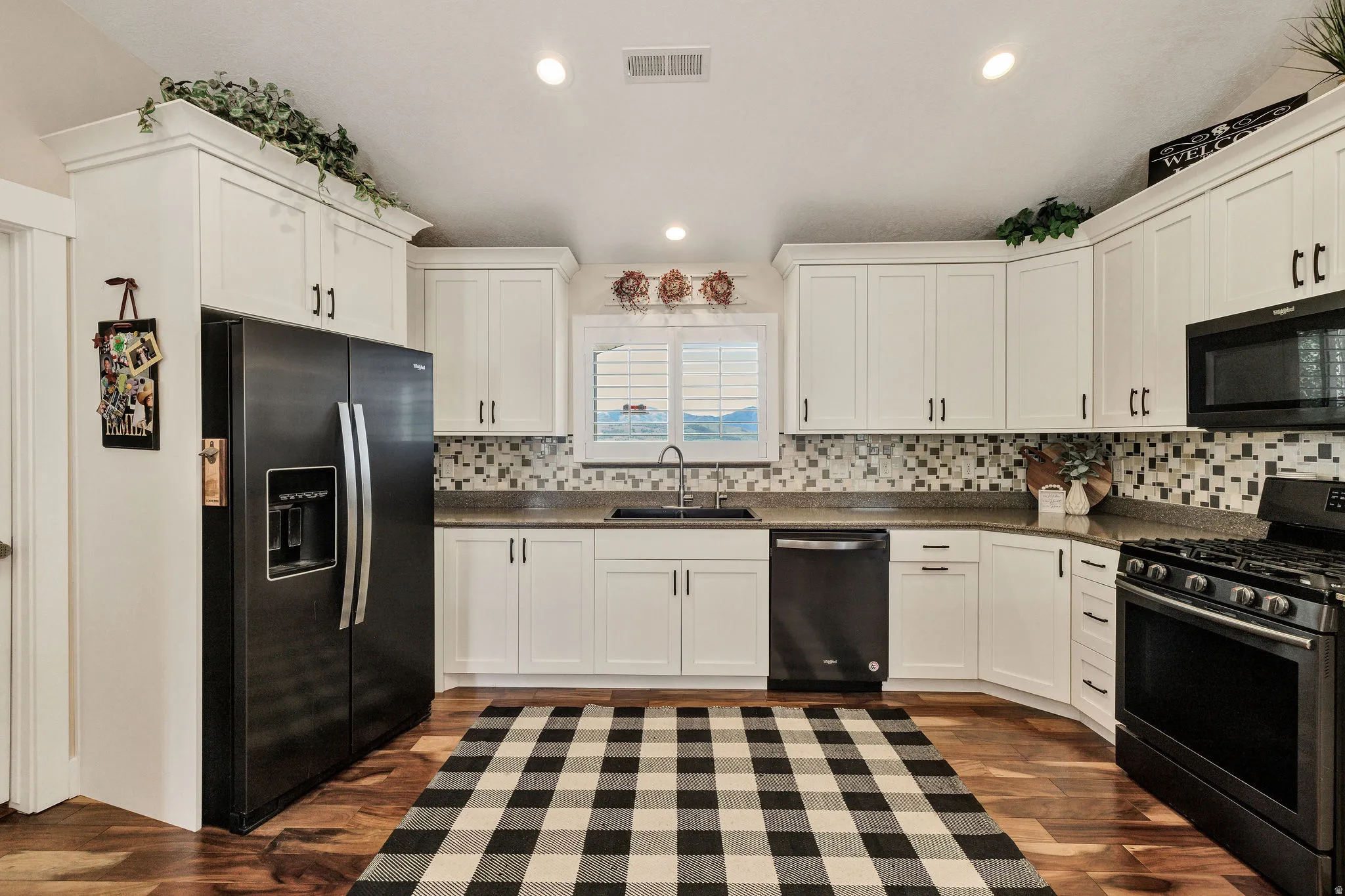 Bright kitchen featuring white shaker cabinetry, dark countertops, a mosaic tile backsplash, black appliances, and wood-finish flooring