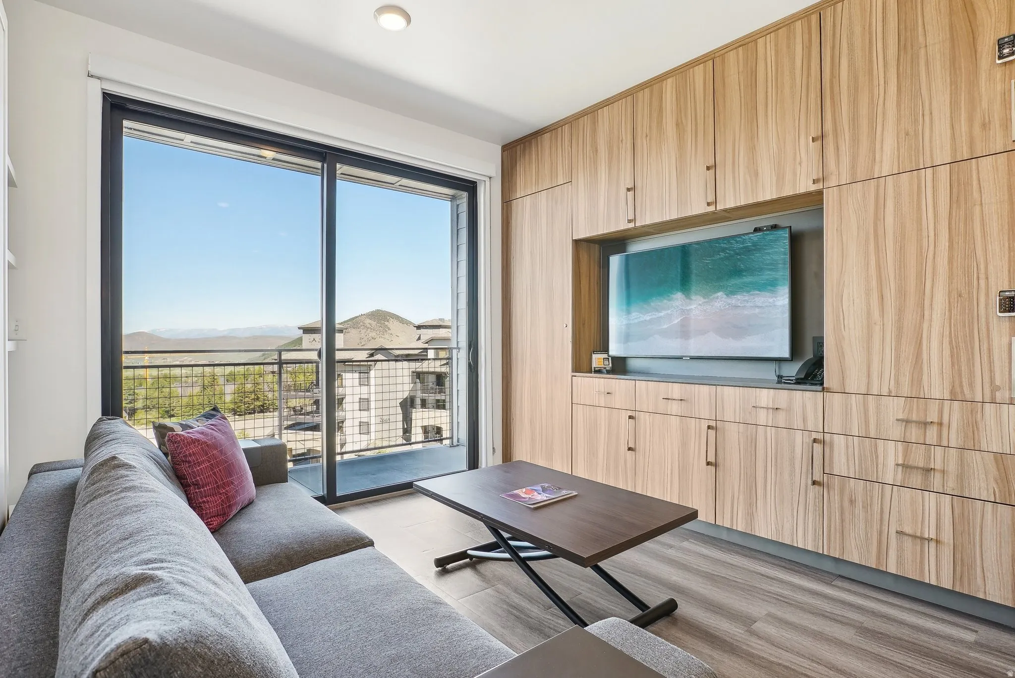 Expansive sliding glass doors provide access to an outdoor balcony with metal railing, featuring distant mountain scenery