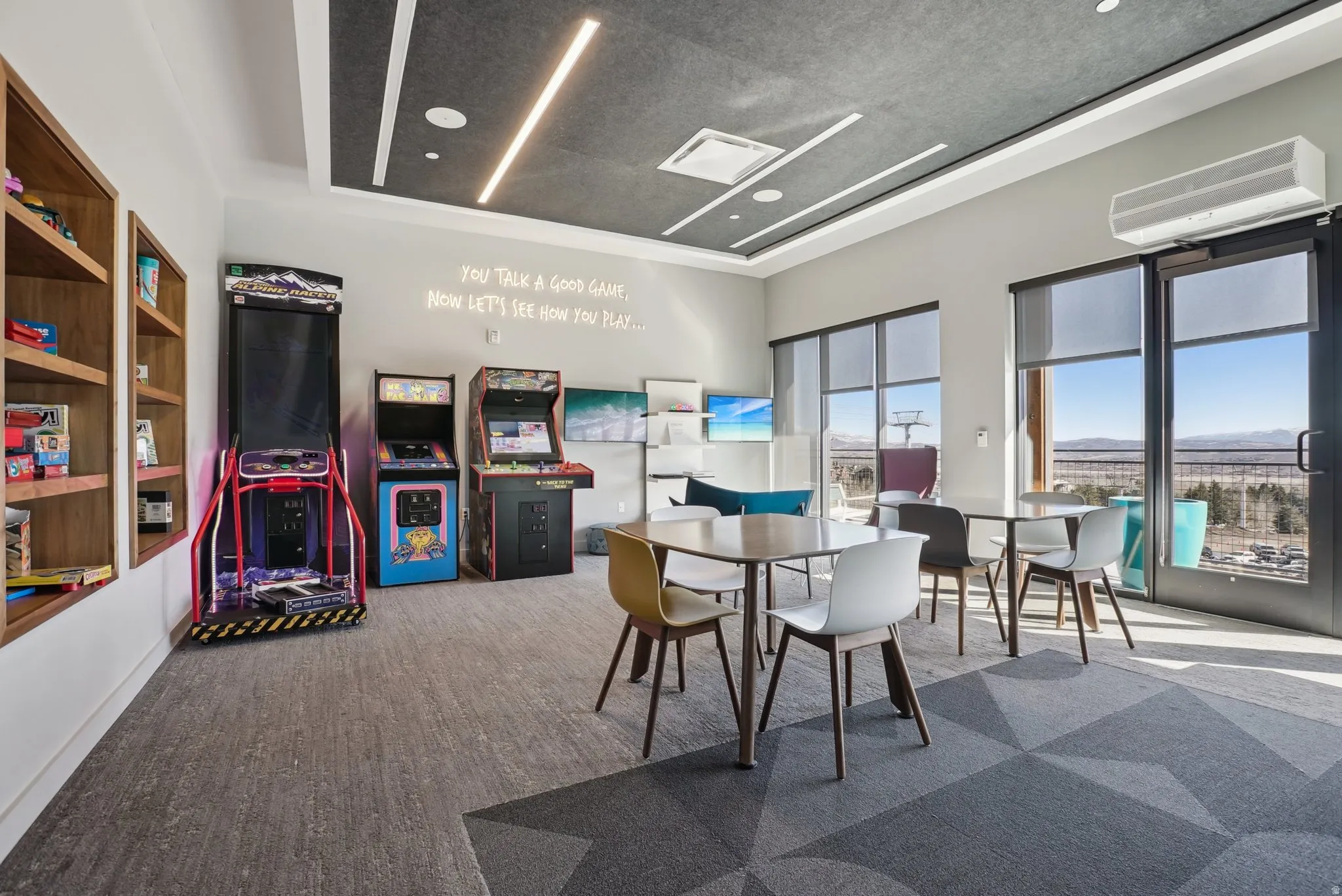 Recreational room featuring a trio of arcade machines, built-in wooden shelving, and patterned carpet flooring