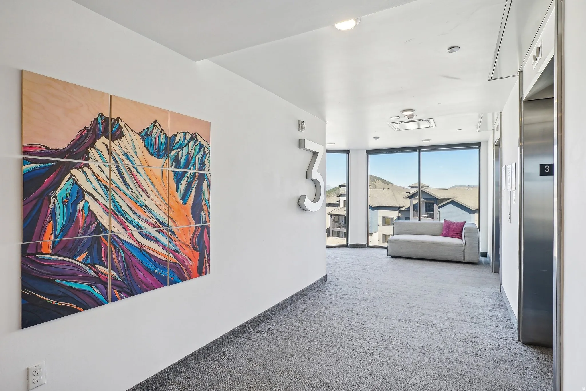 Modern common area featuring floor-to-ceiling windows, mountain scenery, and two stainless steel elevators