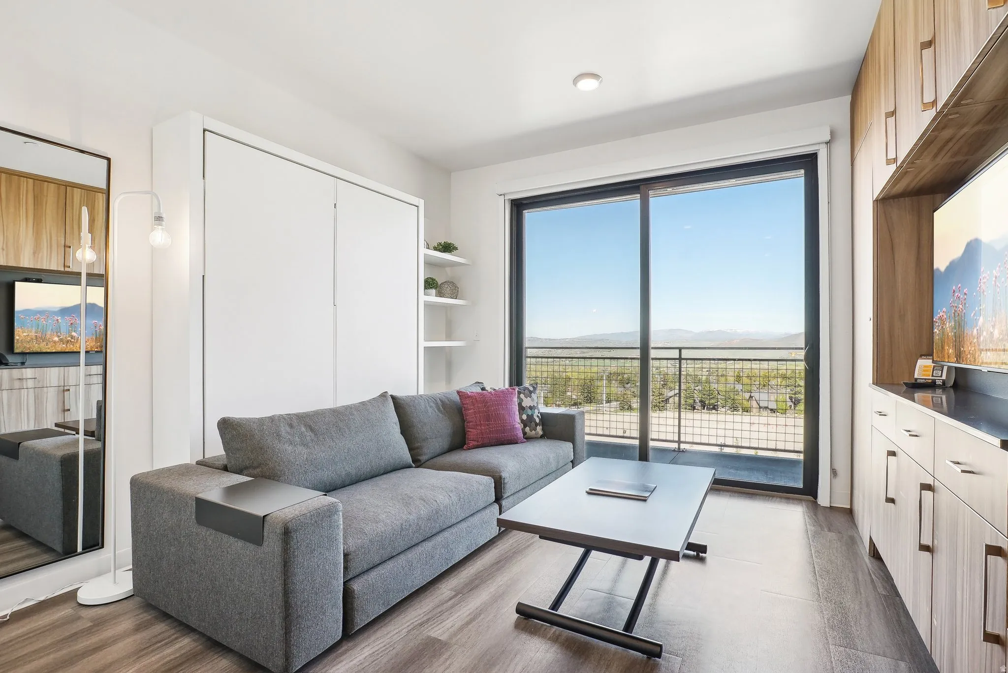 Sliding glass doors opening to an outdoor balcony, wood-finish flooring, built-in cabinetry, recessed lighting, and a wall-mounted storage unit