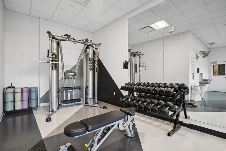 Fitness room featuring wall-mounted mirrors, a multi-station exercise machine, and a dumbbell rack