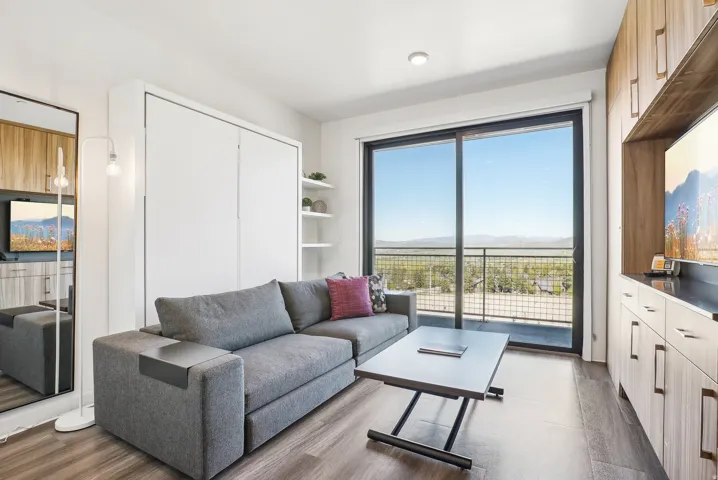 Sliding glass doors opening to an outdoor balcony, wood-finish flooring, built-in cabinetry, recessed lighting, and a wall-mounted storage unit