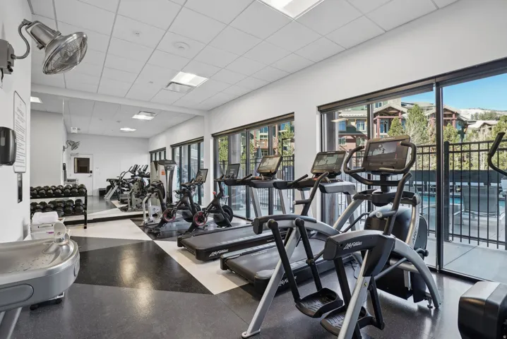 Dedicated fitness center featuring large windows, specialized flooring, recessed lighting, and a mirrored wall