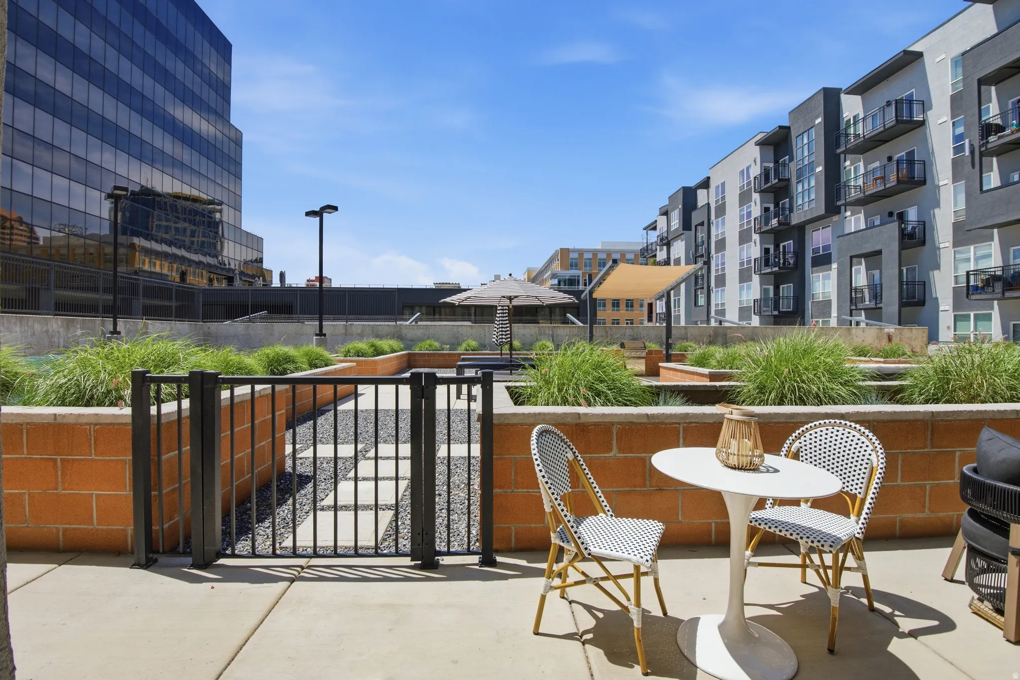 Concrete patio with a low brick wall and black metal fencing opening to a landscaped common area with gravel and paving stones