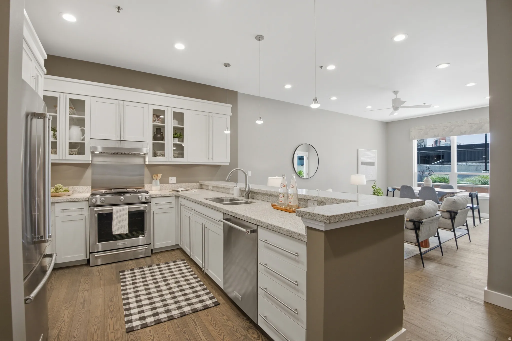 Open-concept kitchen featuring white shaker cabinetry, stainless steel appliances, and wood-finish flooring