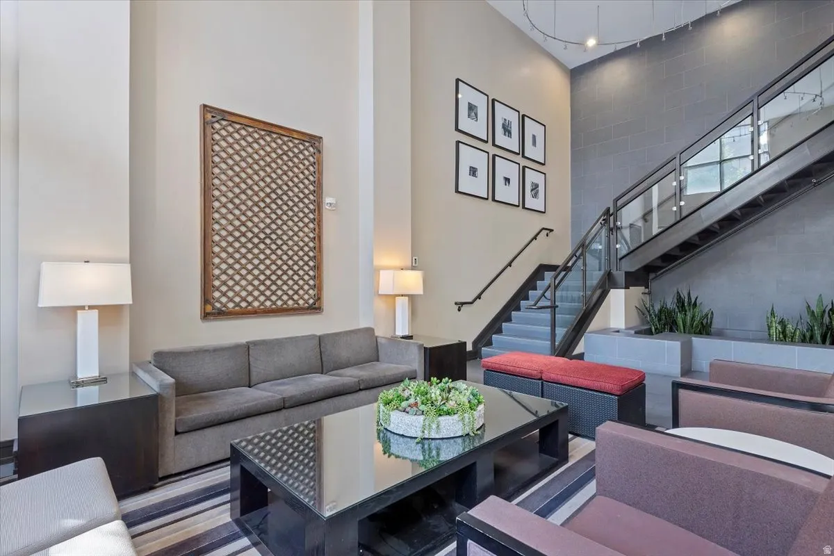Interior lounge area featuring a two-story ceiling, a modern staircase with glass railing, and a tiled accent wall