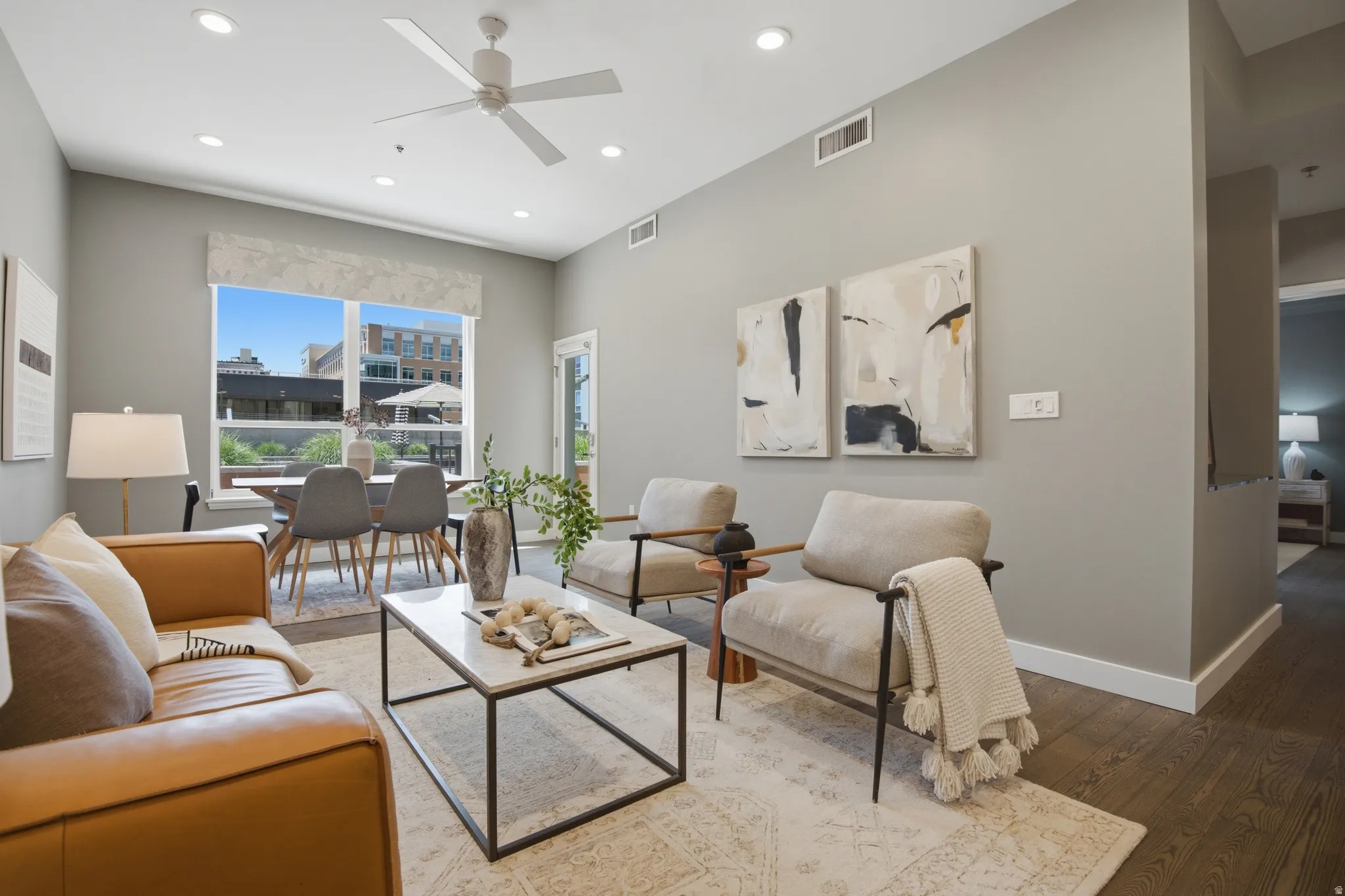 Open-concept living space featuring high ceilings, recessed lighting, wood-finish flooring, and a large window overlooking an outdoor patio