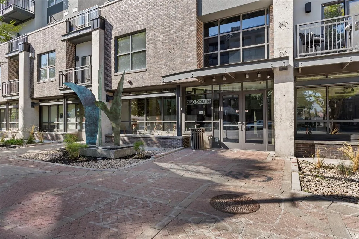 Contemporary building entrance featuring an artistic metal sculpture, brick facade, ground-floor retail windows, and private balconies with metal railings