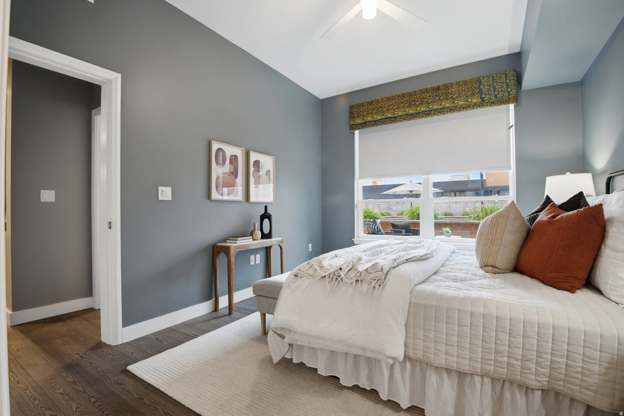 Bedroom featuring wood-finish flooring, a ceiling fan, and a large window with a roller shade