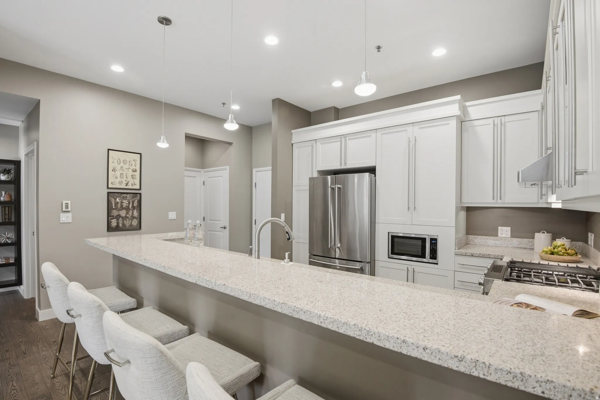 Kitchen featuring a large breakfast bar with light-colored countertop, stainless steel appliances, white cabinetry with crown molding, recessed lighting, and pendant lighting fixtures