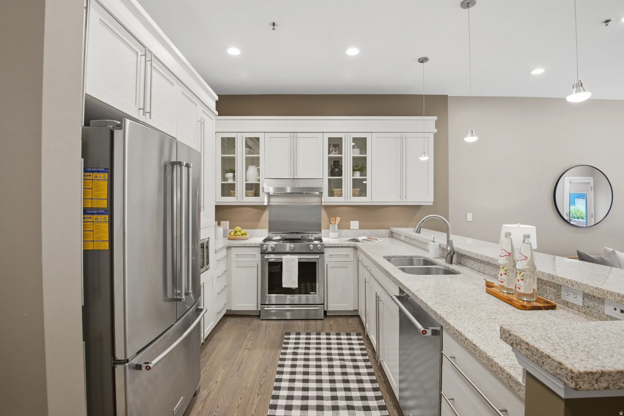 Well-appointed kitchen featuring a stainless steel appliance suite, white shaker cabinetry, stone-finish countertops, wood-finish flooring, and recessed lighting