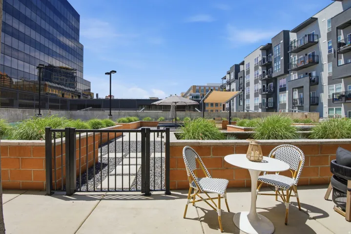 Concrete patio with a low brick wall and black metal fencing opening to a landscaped common area with gravel and paving stones