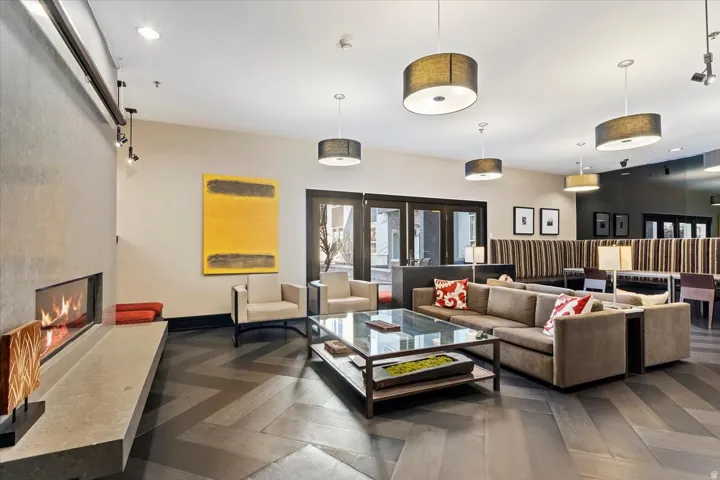 Spacious common area featuring a modern fireplace with a substantial hearth, herringbone wood-finish flooring, multiple drum pendant light fixtures, and double glass-paneled doors