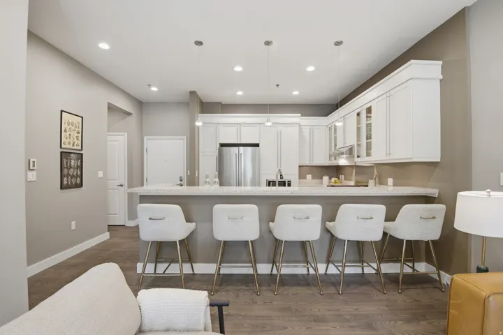Modern kitchen featuring an expansive island with seating, stainless steel appliances, white cabinetry, and wood-finish flooring