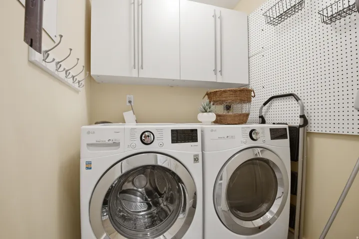 Laundry area featuring upper white cabinetry, a white pegboard wall, and light neutral wall paint
