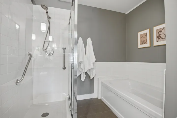 Bathroom featuring a glass-enclosed shower with white subway tile, an integrated shower bench, and grab bars