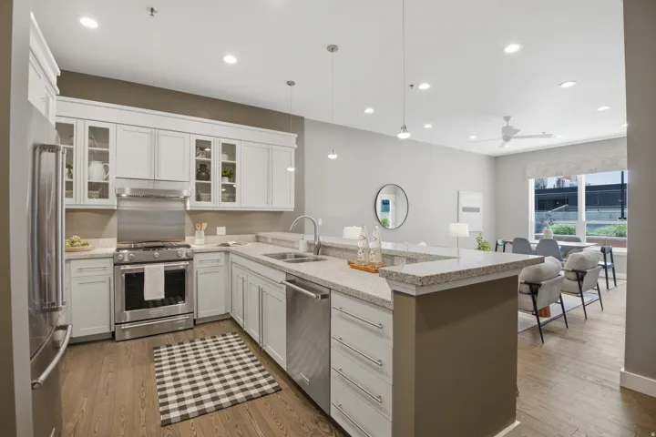 Open-concept kitchen featuring white shaker cabinetry, stainless steel appliances, and wood-finish flooring