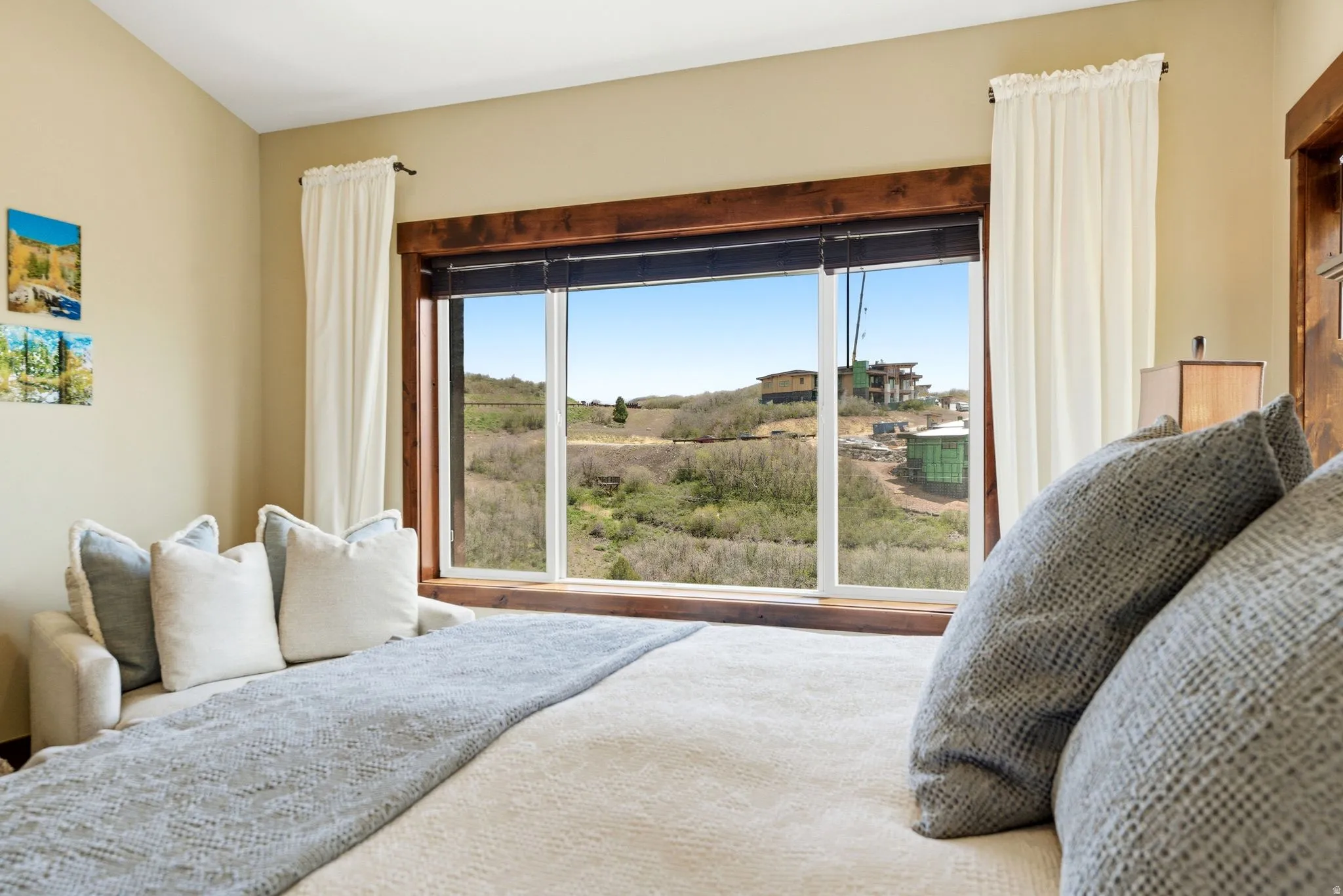 Expansive picture window with dark wood trim and white casing, showcasing distant architectural properties and natural outdoor landscaping