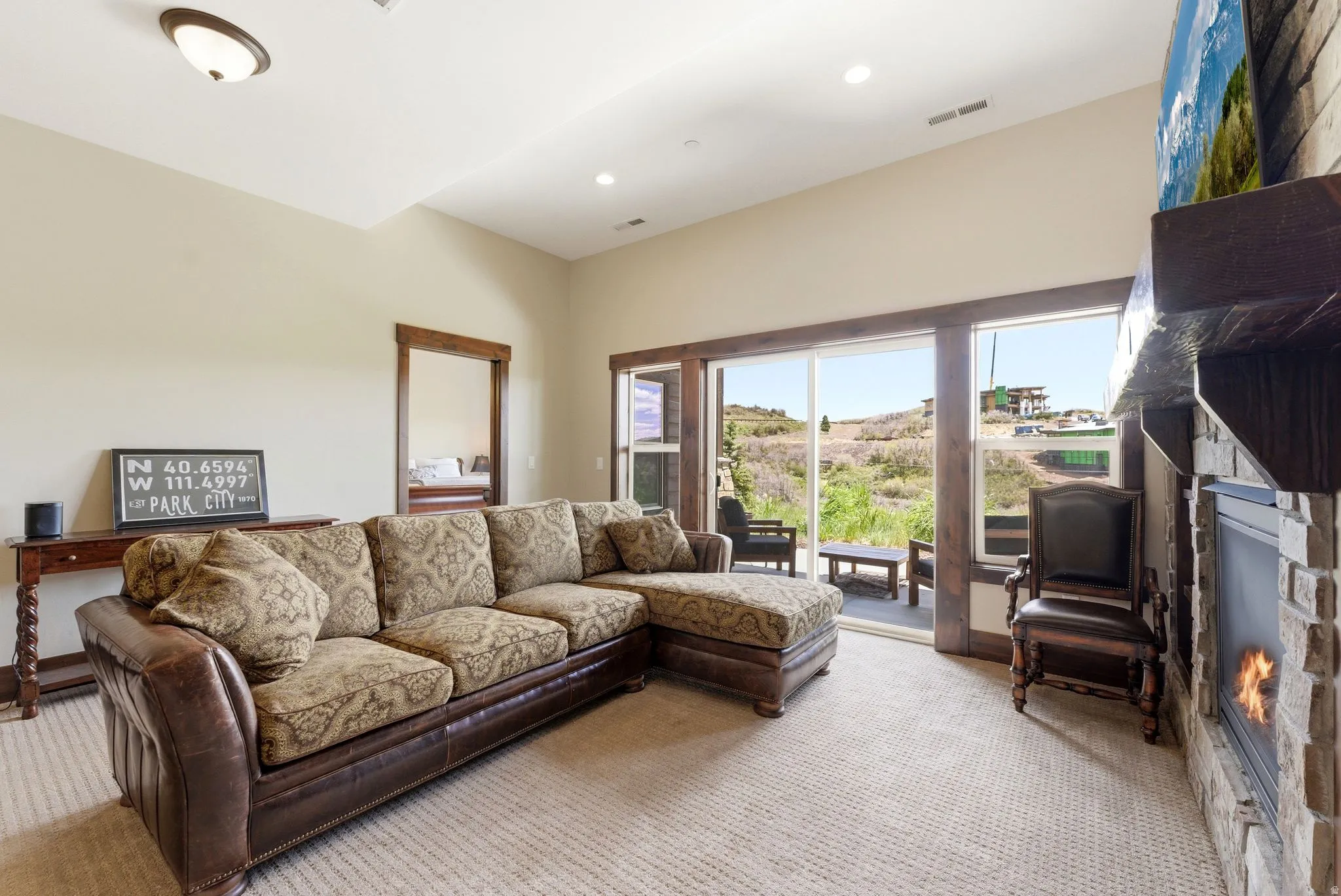 Living area featuring a stone-clad fireplace with wood mantel, sliding glass door access to an exterior patio, recessed ceiling lighting, and a neutral carpet
