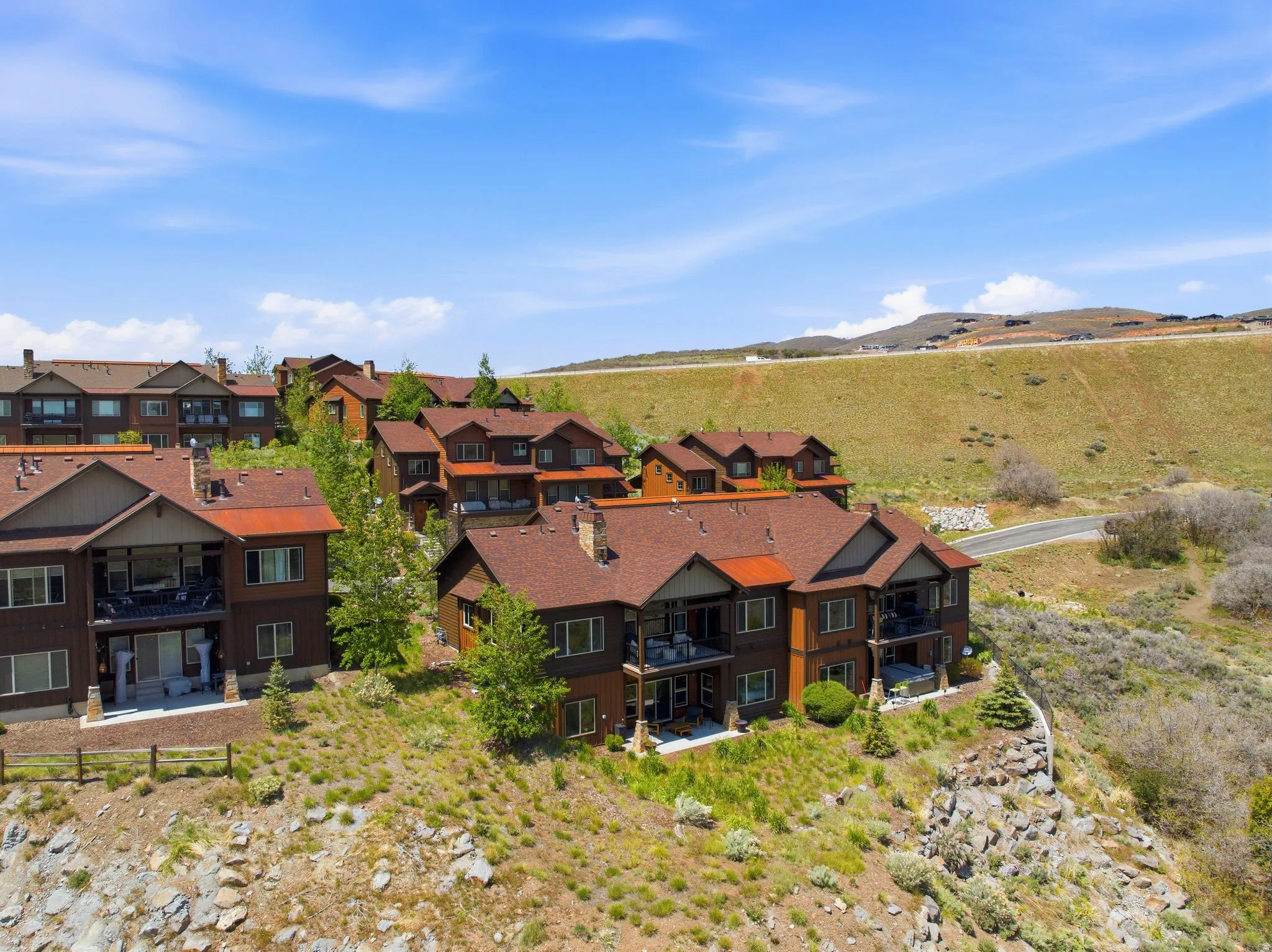 Terraced residential structures featuring multiple balconies and patios, situated on a hillside with natural landscaping