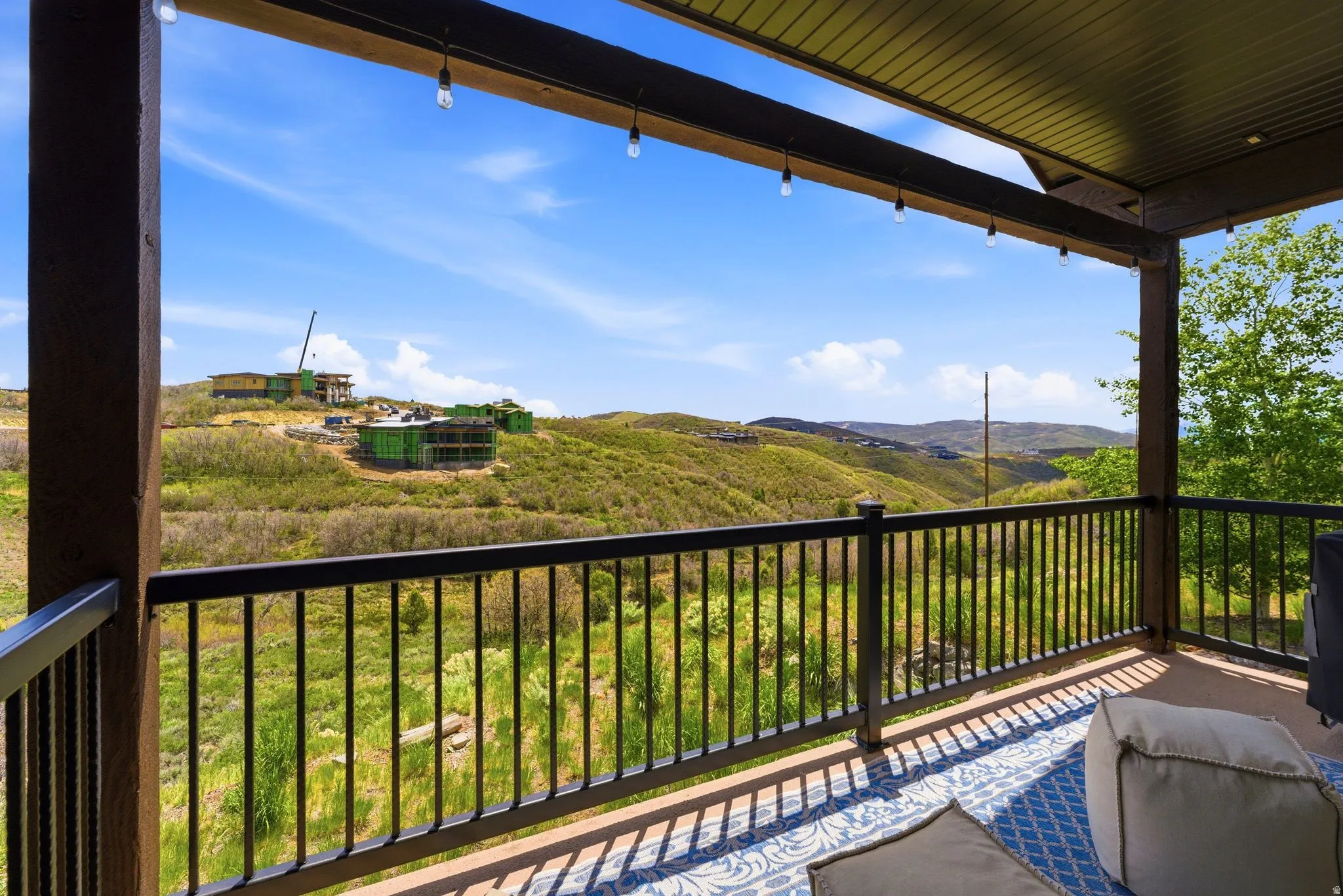 Covered outdoor patio featuring exposed wood beams, string lighting, and a black metal railing