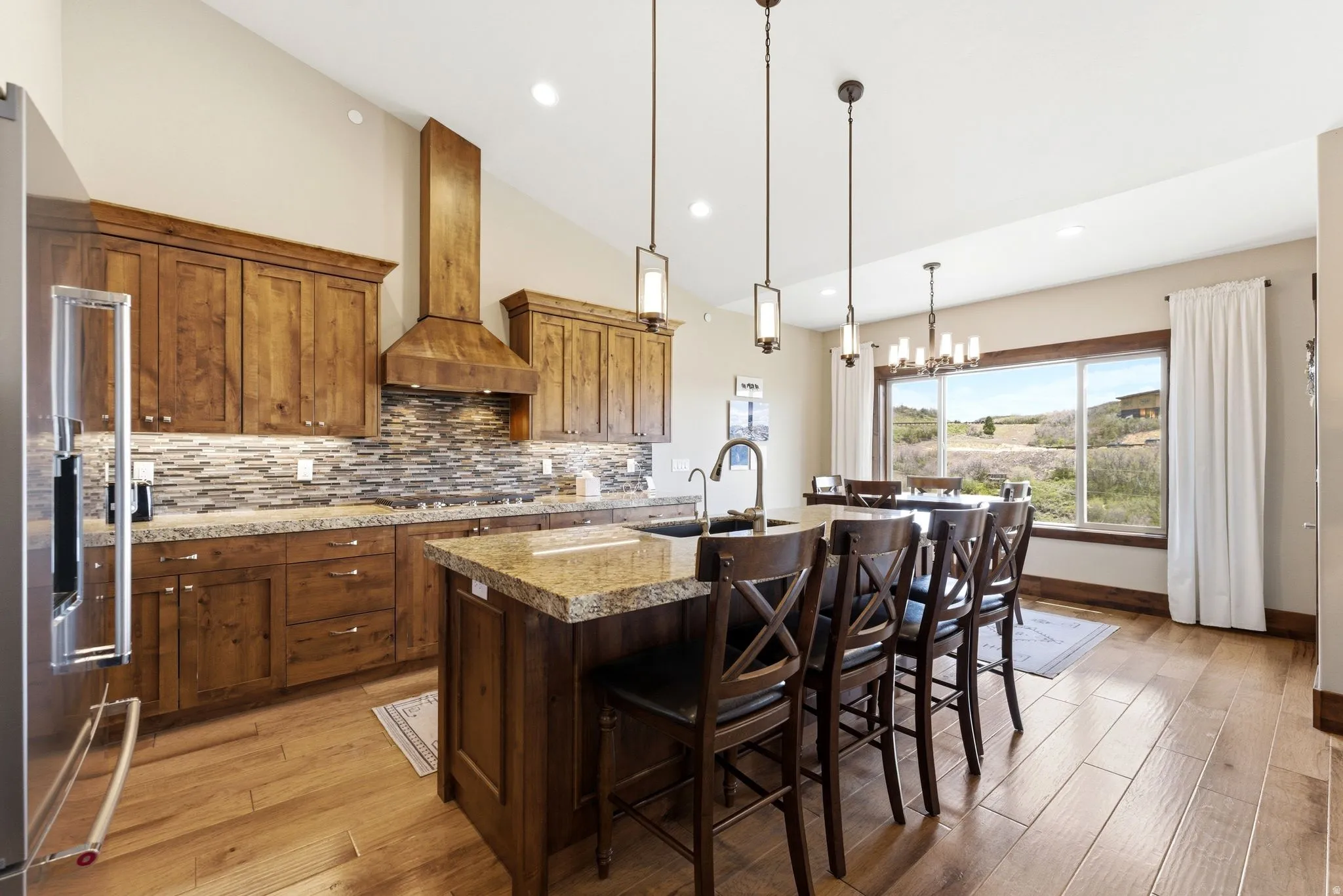 Spacious kitchen featuring wood-finish flooring, granite countertops, a large island with sink, stainless steel refrigerator, and a tiled backsplash