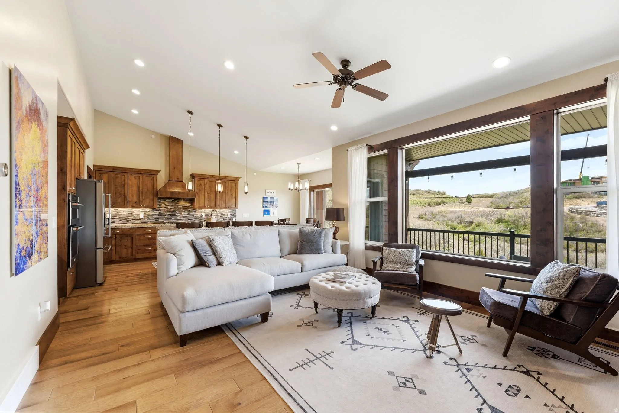 Open-concept living space featuring wood-finish flooring, vaulted ceilings with recessed lighting, and a kitchen with stainless steel appliances and wood cabinetry