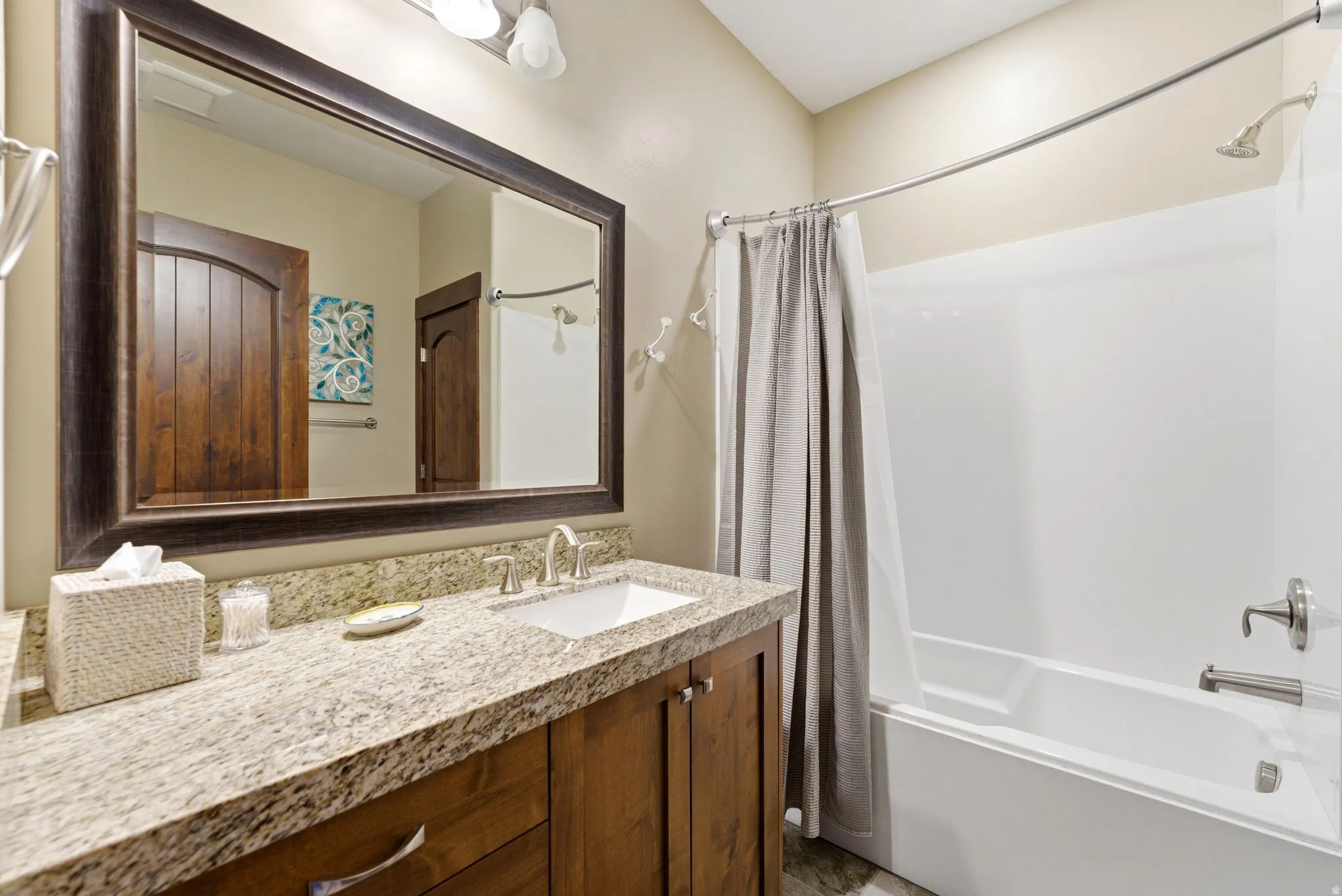 Bathroom featuring a wood-finish vanity with an integrated sink, granite-style countertop, and a large framed mirror