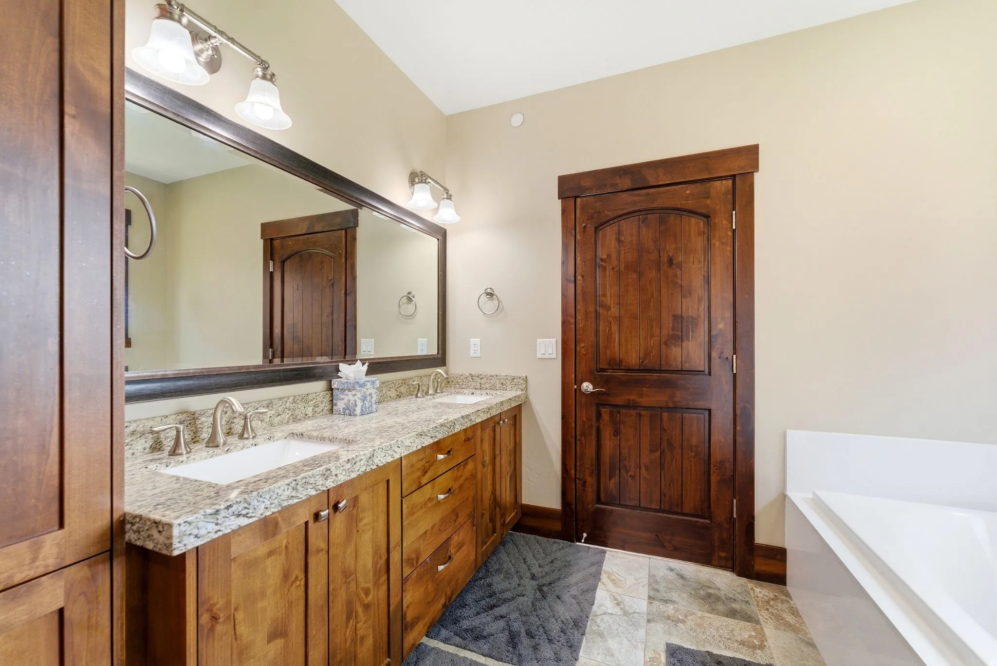 Double vanity featuring undermount sinks, granite-style countertops, and wood-finish cabinetry