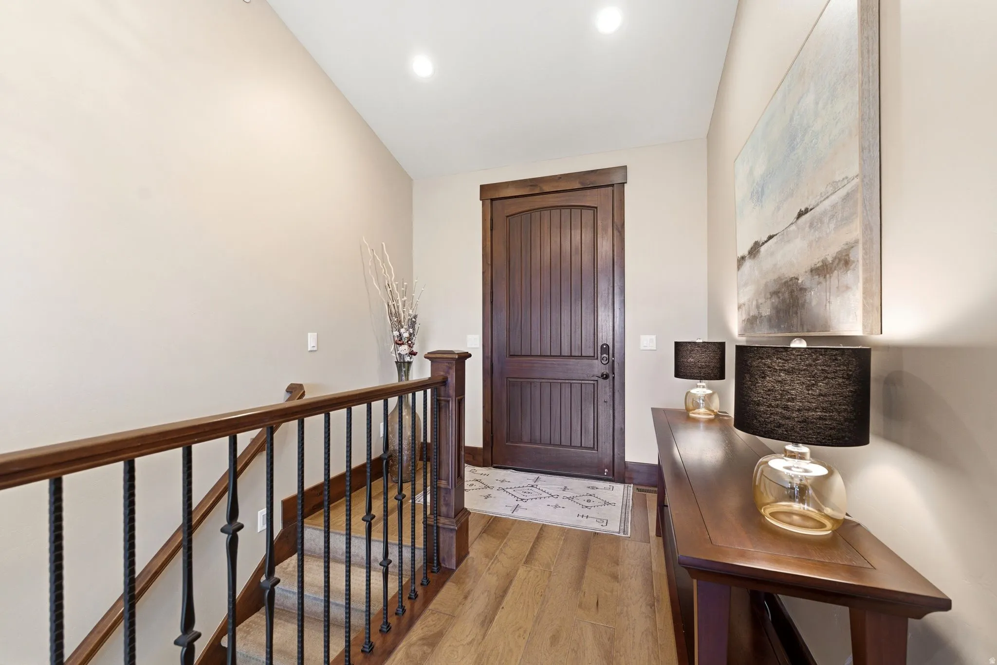 Entryway featuring a solid wood door with vertical paneling, light wood-finish flooring, a dark wood handrail, and wrought iron balusters