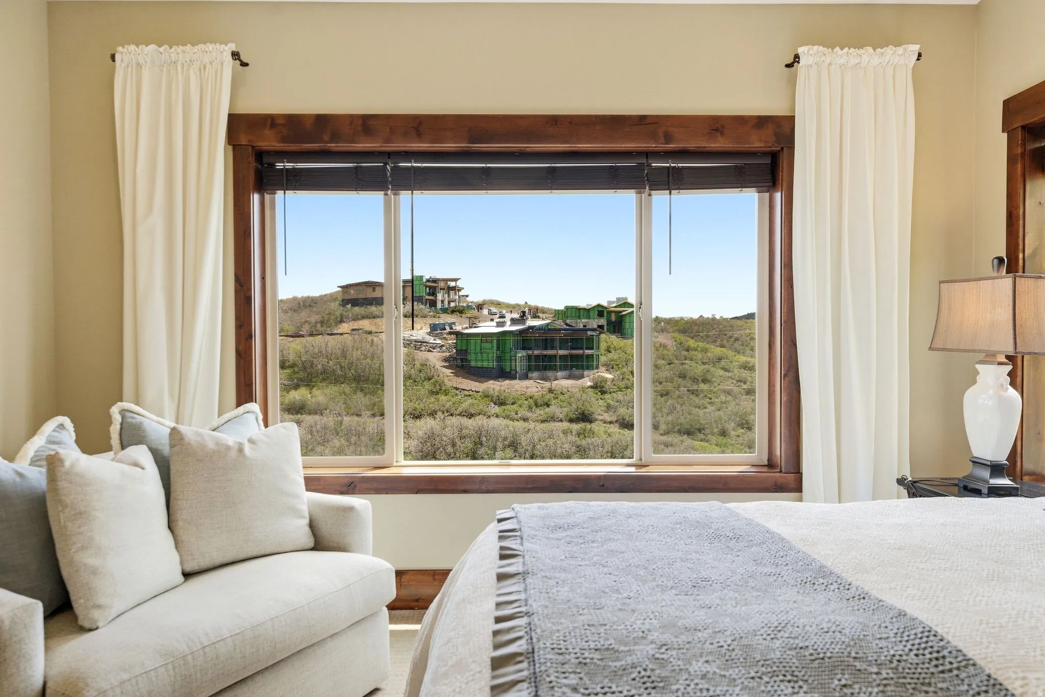 Expansive picture window framed by rich wood trim and neutral curtains, offering sweeping hillside and distant property views