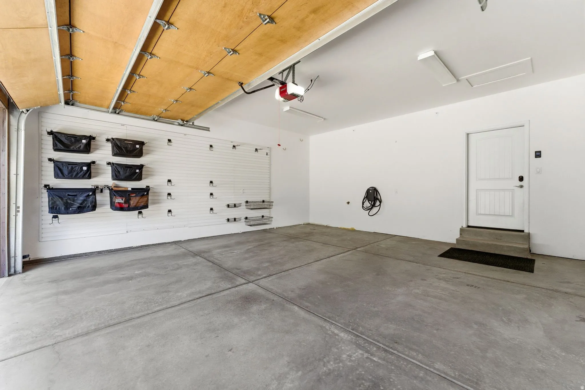 Spacious garage featuring a concrete floor, slatwall organization system, overhead lighting, and an internal access door