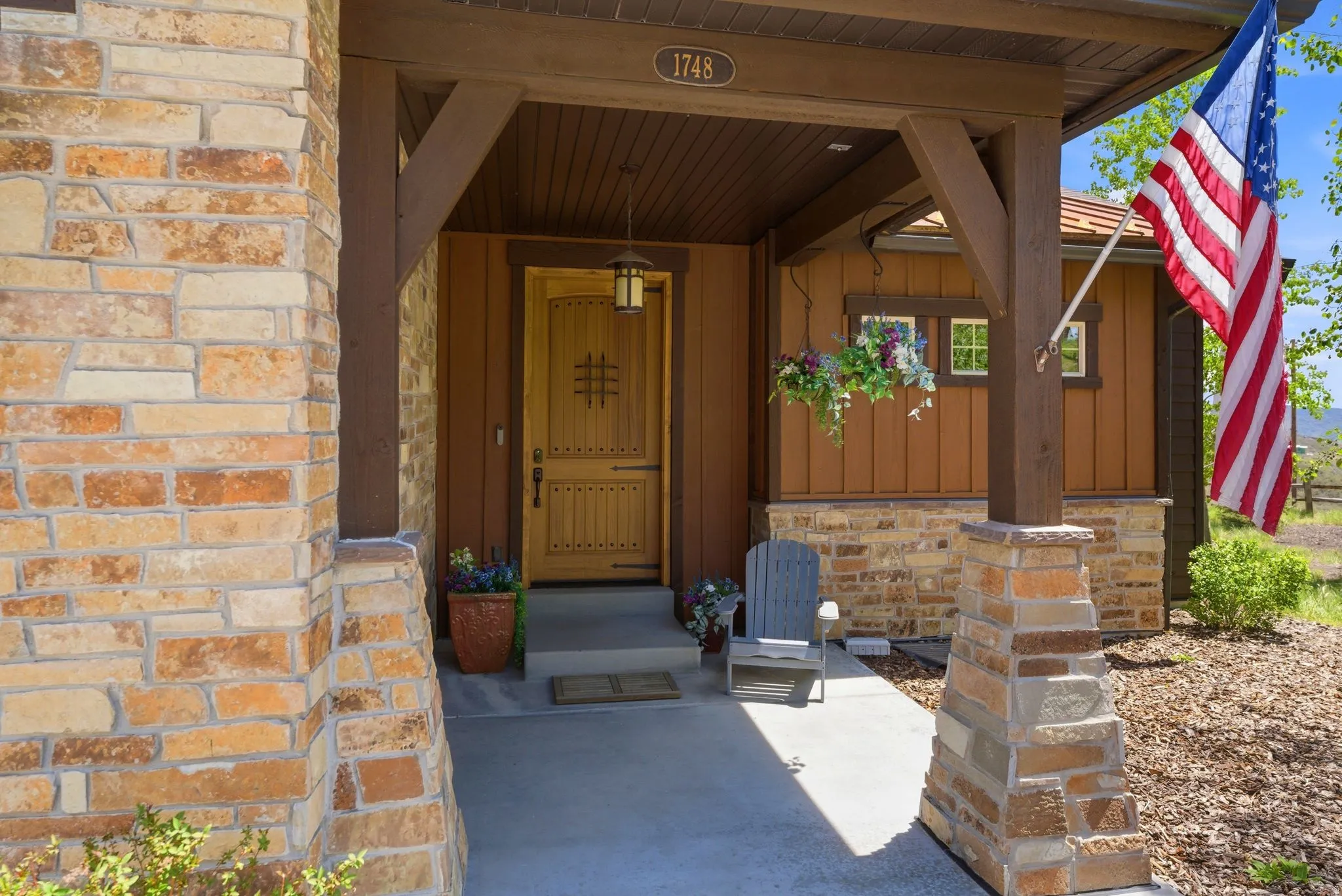 Craftsman-style entry with a custom wood door, stone facade accents, and exposed timber beams