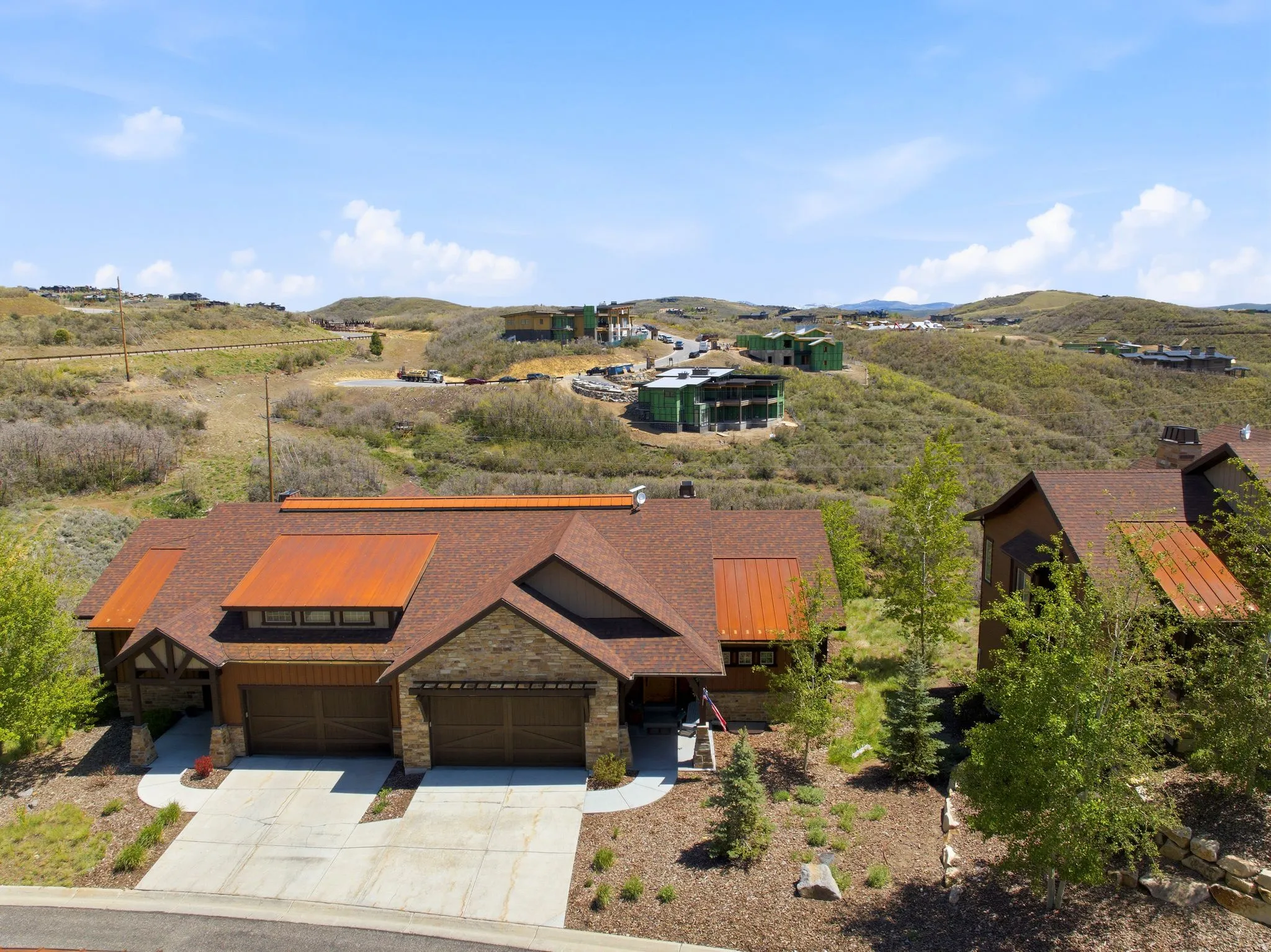 Stone and wood-sided exterior featuring a multi-gabled shingle roof with metal accents, two distinct garage doors, and a concrete driveway